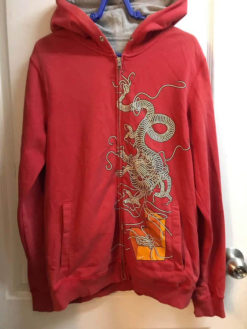 Red Hoodie 桌布 壁紙 — 一件紅色拉鍊連帽上衣，上面有精緻的白色龍圖案，掛在藍色衣架上，背景是白色門。