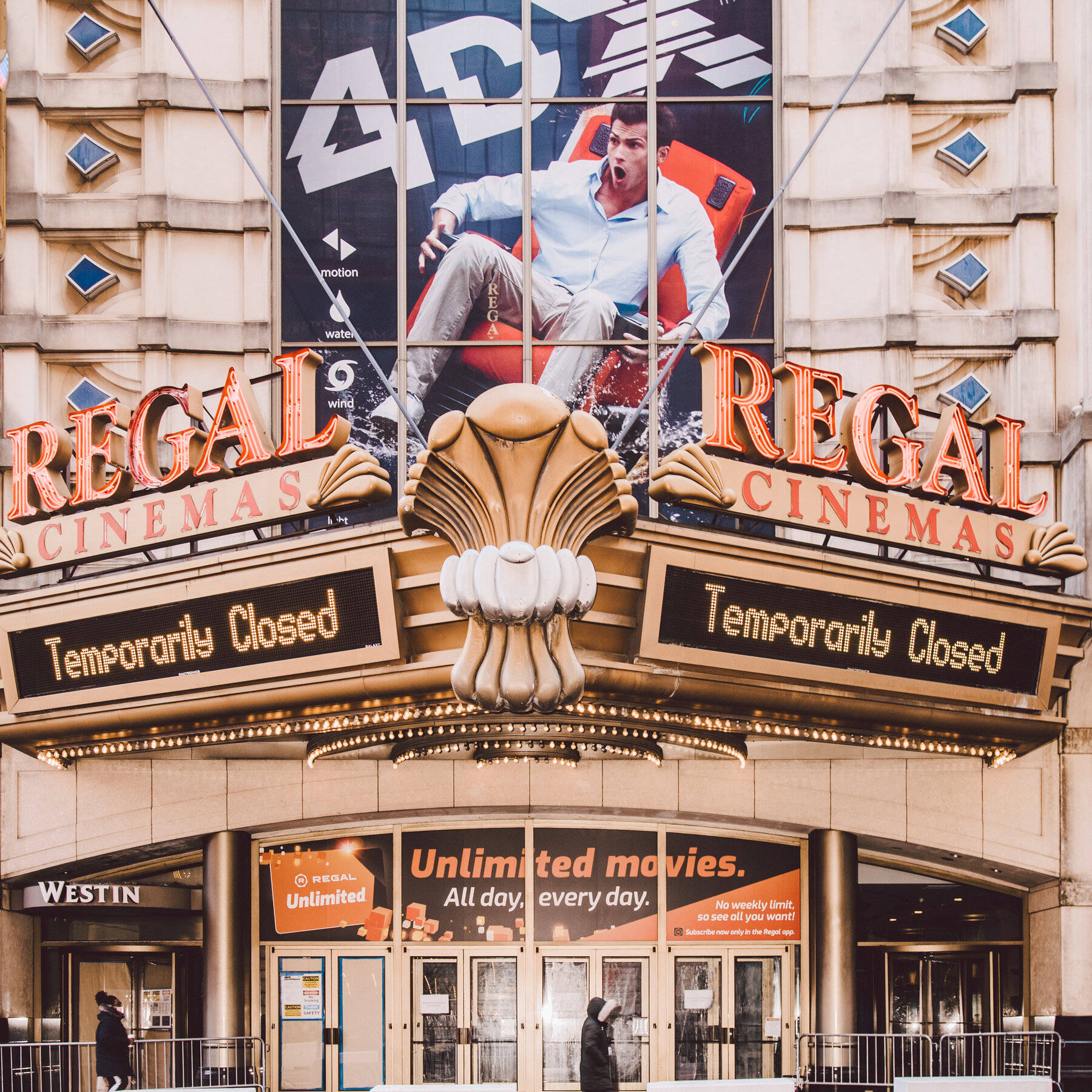 Regal 桌布 壁紙 — Regal Cinemas 戲院外牆，帶有「暫時關閉」標誌和一個男人坐在紅色椅子上的大型電影海報。