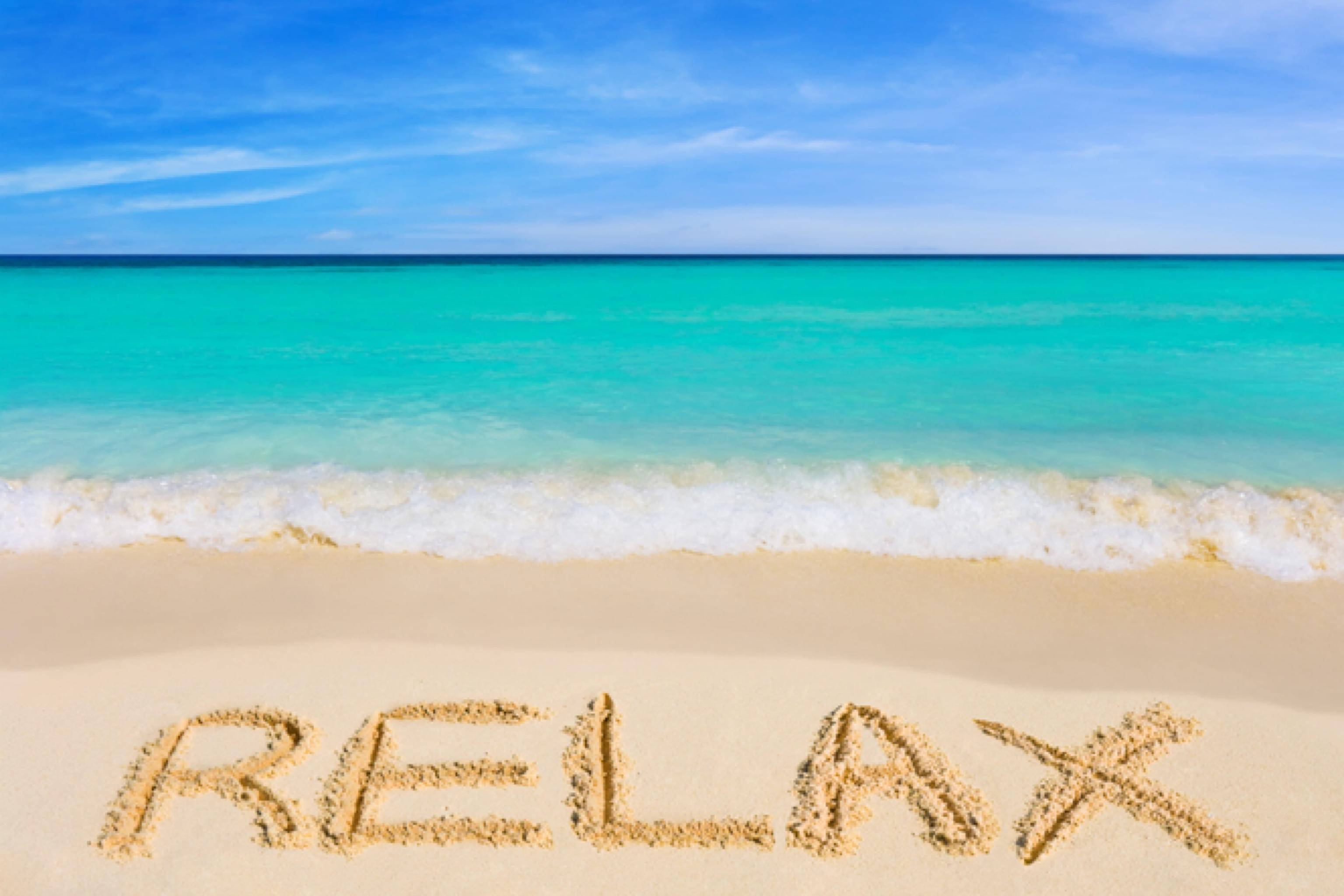View 桌布 壁紙 — 「RELAX」這個字寫在陽光沙灘的沙上，在晴朗藍天之下，有藍綠色海浪湧過來。