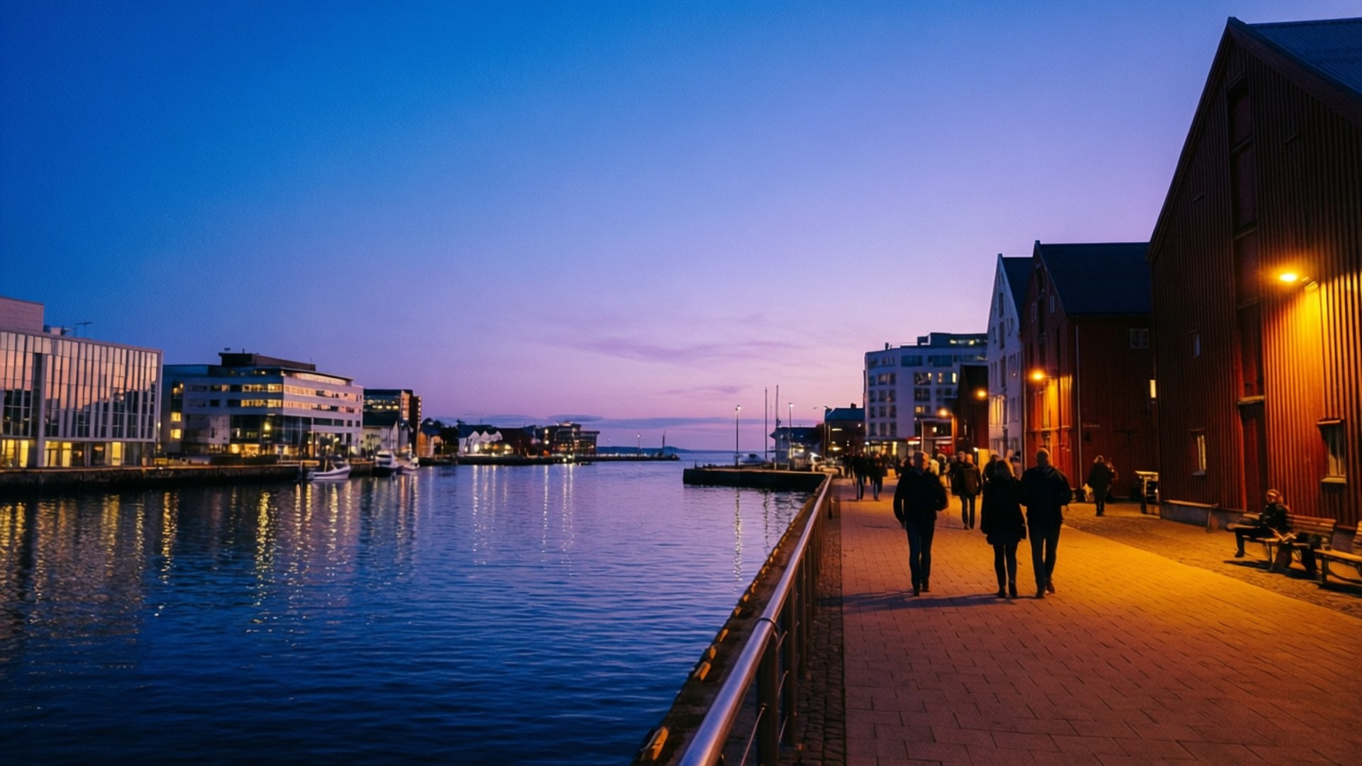 Haugesund 桌布 壁紙 — 人們在黃昏時分沿著溫暖燈光照亮的海濱長廊漫步，城市燈光在紫藍色天空下的平靜水面上反射。