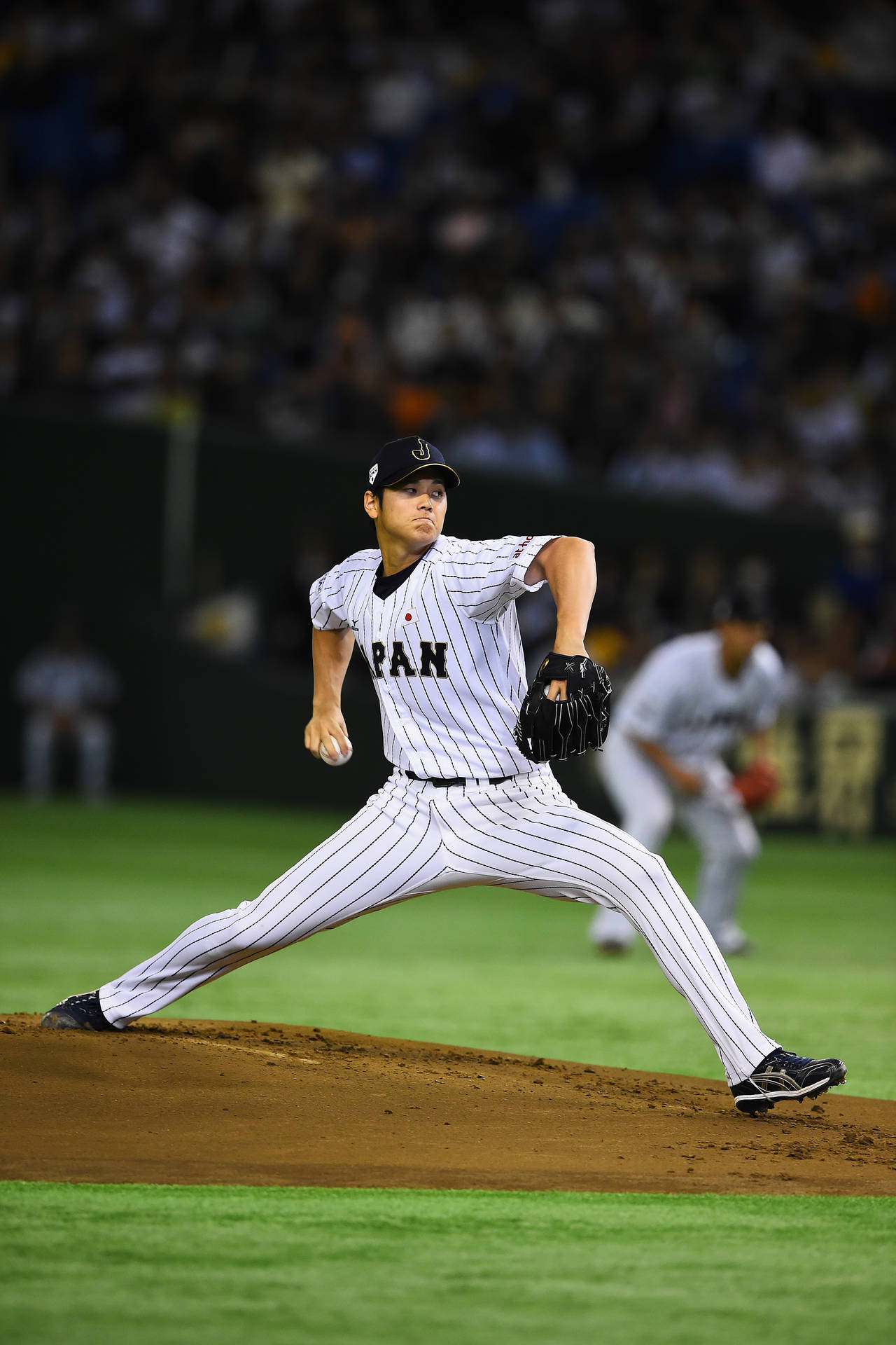 穿著條紋制服的棒球投手在夜間燈光下投球中。 — MLB 壁紙