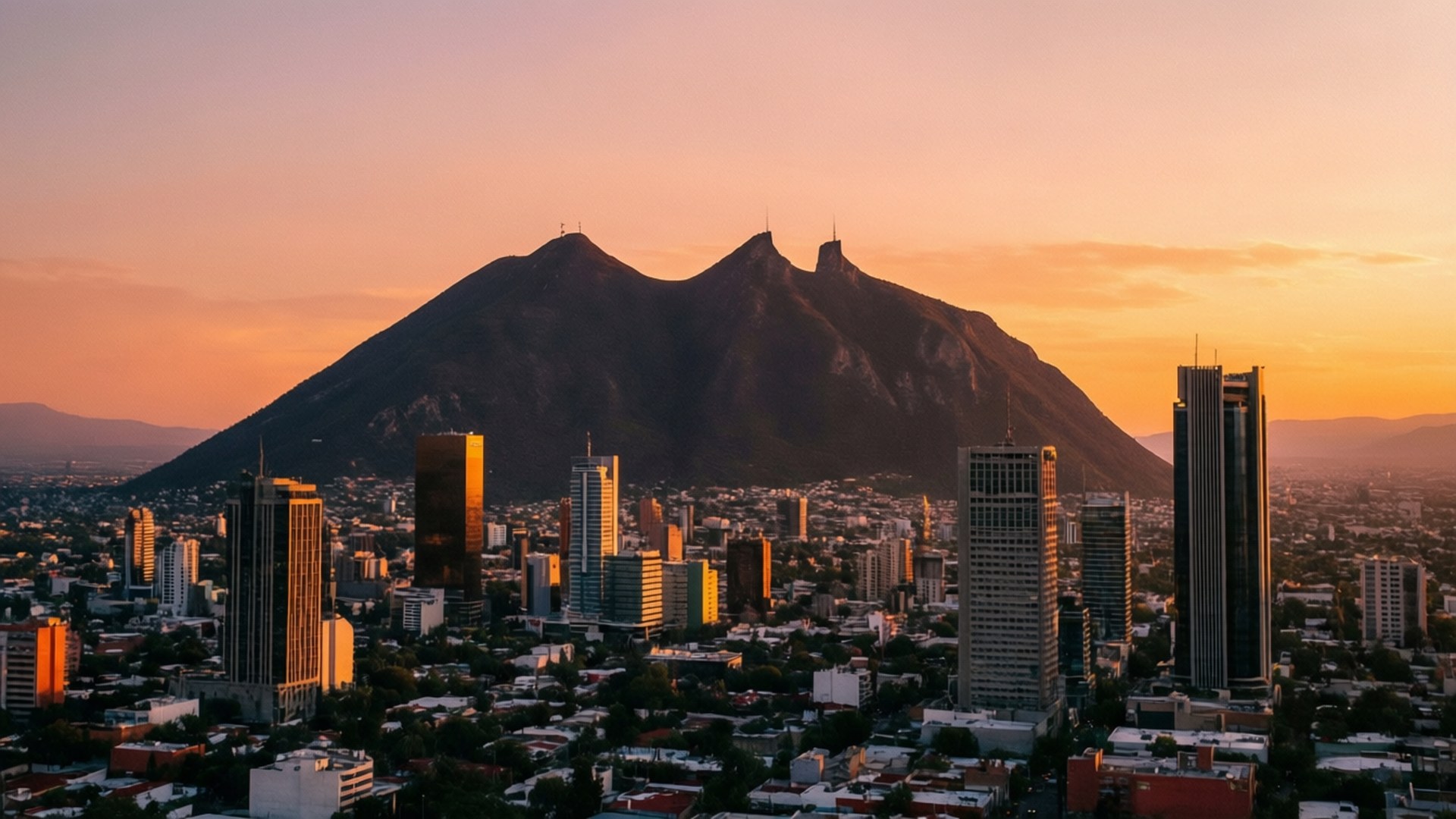 Monterrey Skyline Sunset 壁紙 — 日落時分的城市景觀，高聳的摩天大樓和背景中的大山沐浴在溫暖的橙色光芒中。