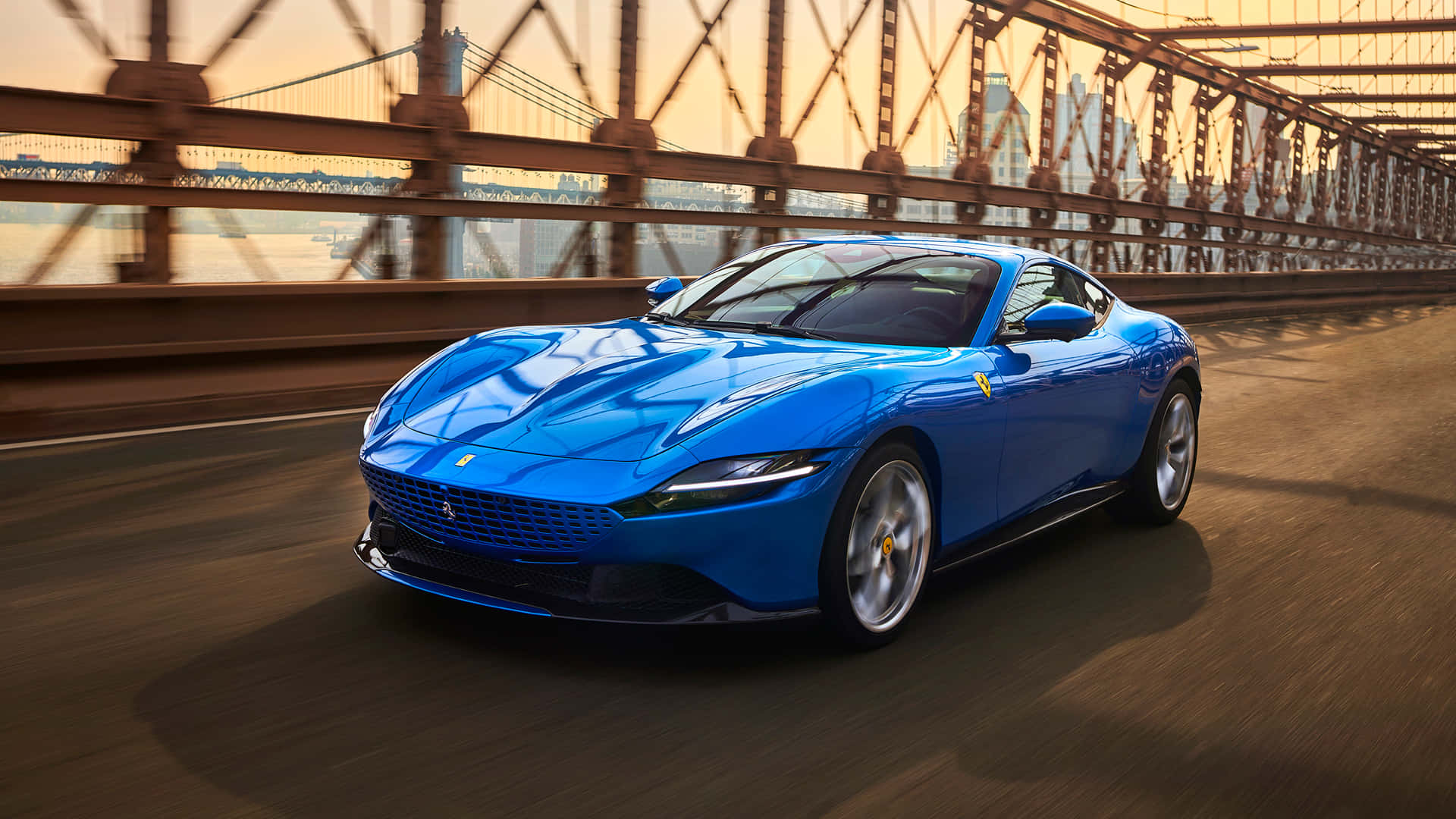 Ferrari Roma 桌布 壁紙 — 一輛充滿活力的藍色法拉利跑車在金色光線下，帶著動態模糊效果飛馳過一座鋼橋。