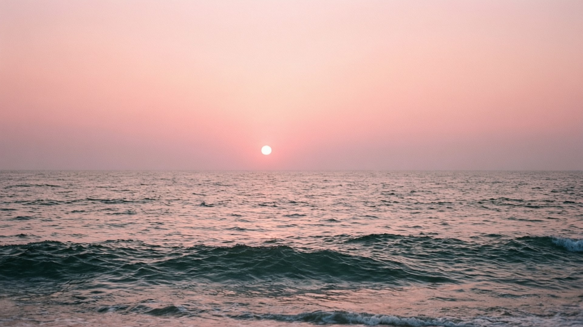 Pink Ocean Sunset 壁紙 — 日落時分寧靜的海洋，地平線上閃耀的太陽在平靜的水面上投下粉紅色調。
