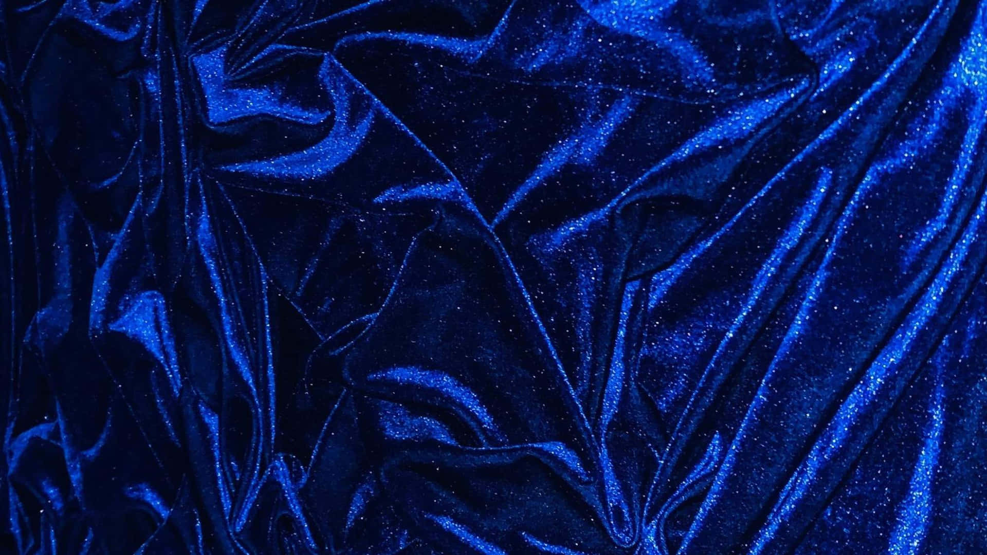  壁紙 — 豐富的皇家藍色天鵝絨布料，在戲劇性燈光下呈現閃爍質感和深層皺褶。
