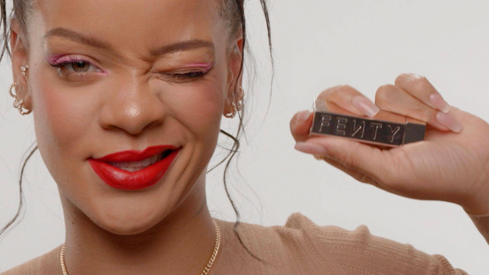 Fenty 桌布 壁紙 — Rihanna 俏皮地眨眼，手持黑色Fenty唇膏，搭配大膽紅唇和粉紅色眼線。