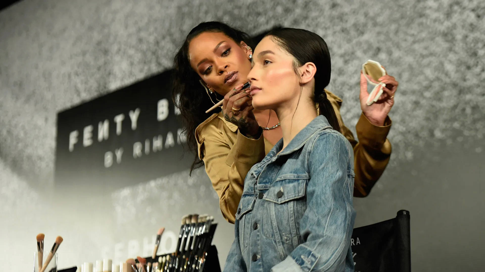 Fenty 桌布 壁紙 — Rihanna 在 Fenty Beauty 活動中為模特兒化妝，可見刷具和產品。
