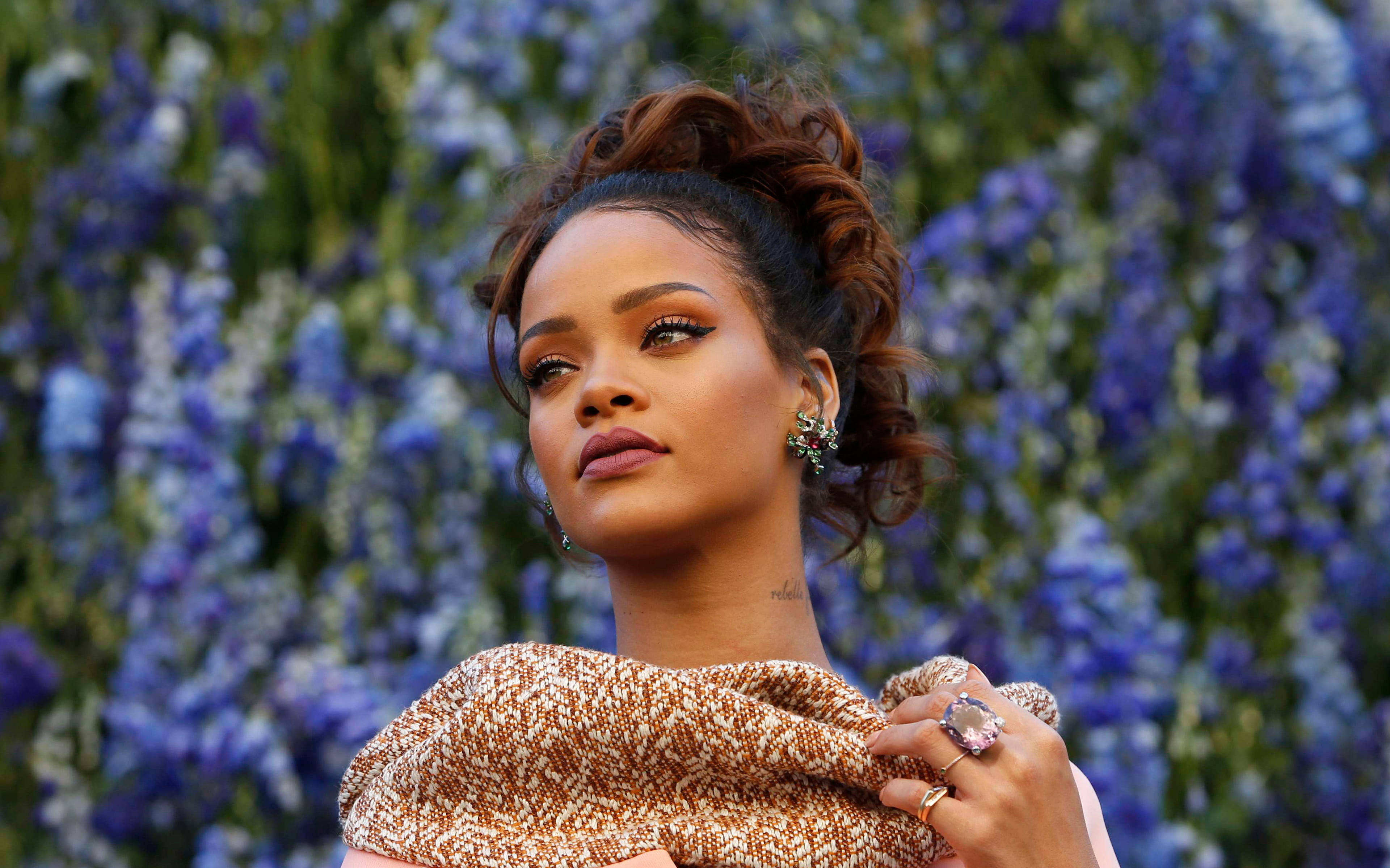Celebrity 桌布 壁紙 — Rihanna 在柔和自然光線下，以鮮豔的藍白色花朵為背景，若有所思地凝視著。