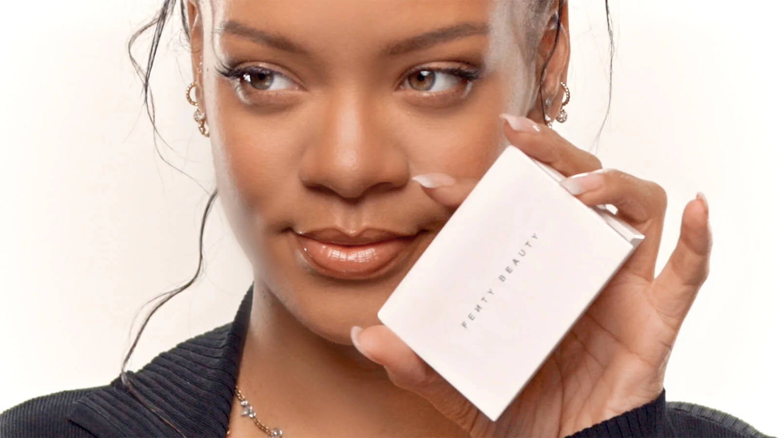 Fenty 桌布 壁紙 — Rihanna 在純色背景前，帶著微妙的微笑，拿著一個白色 Fenty Beauty 粉盒。