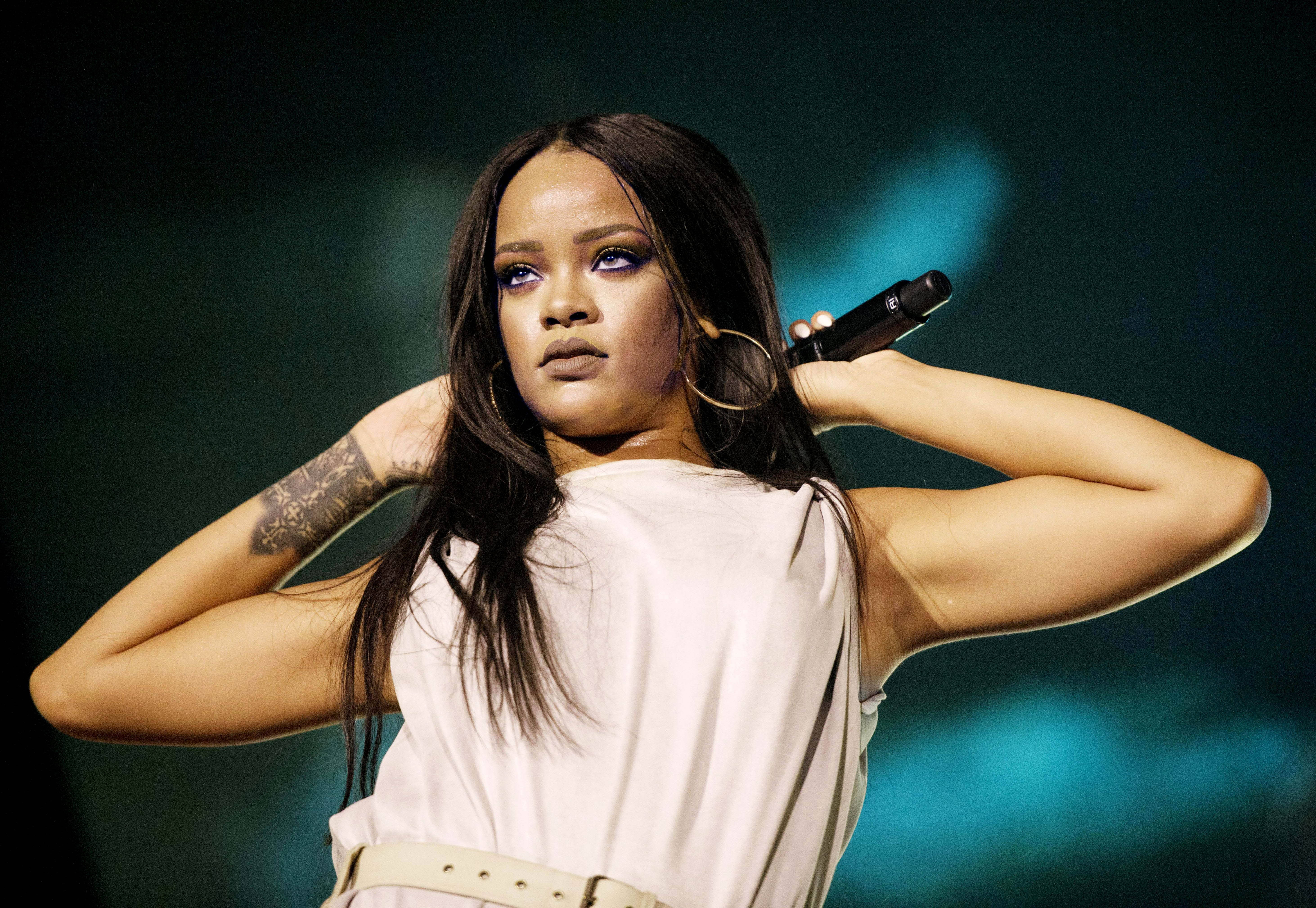 Celebrity 桌布 壁紙 — Rihanna 在舞台上手持麥克風表演，眼神專注，背後有戲劇性的藍色燈光。