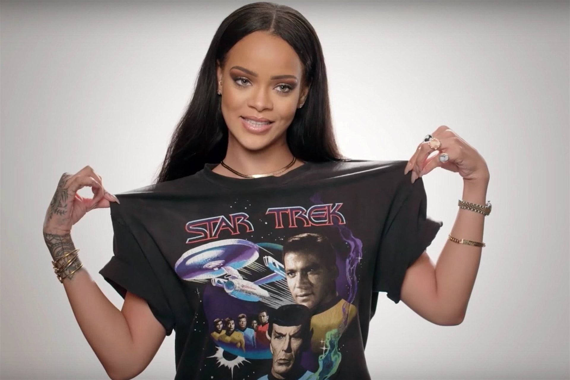 Celebrity 桌布 壁紙 — Rihanna 微笑著舉起一件黑色 Star Trek T恤，上面有企業號和船員，背景是宇宙。