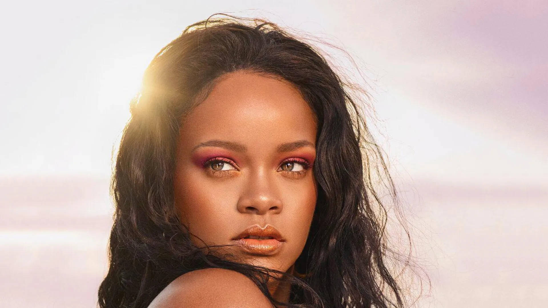 Fenty 桌布 壁紙 — Rihanna 的燦爛肖像，肌膚發光，大膽的粉紅色眼影，襯托柔和的粉彩天空背景。