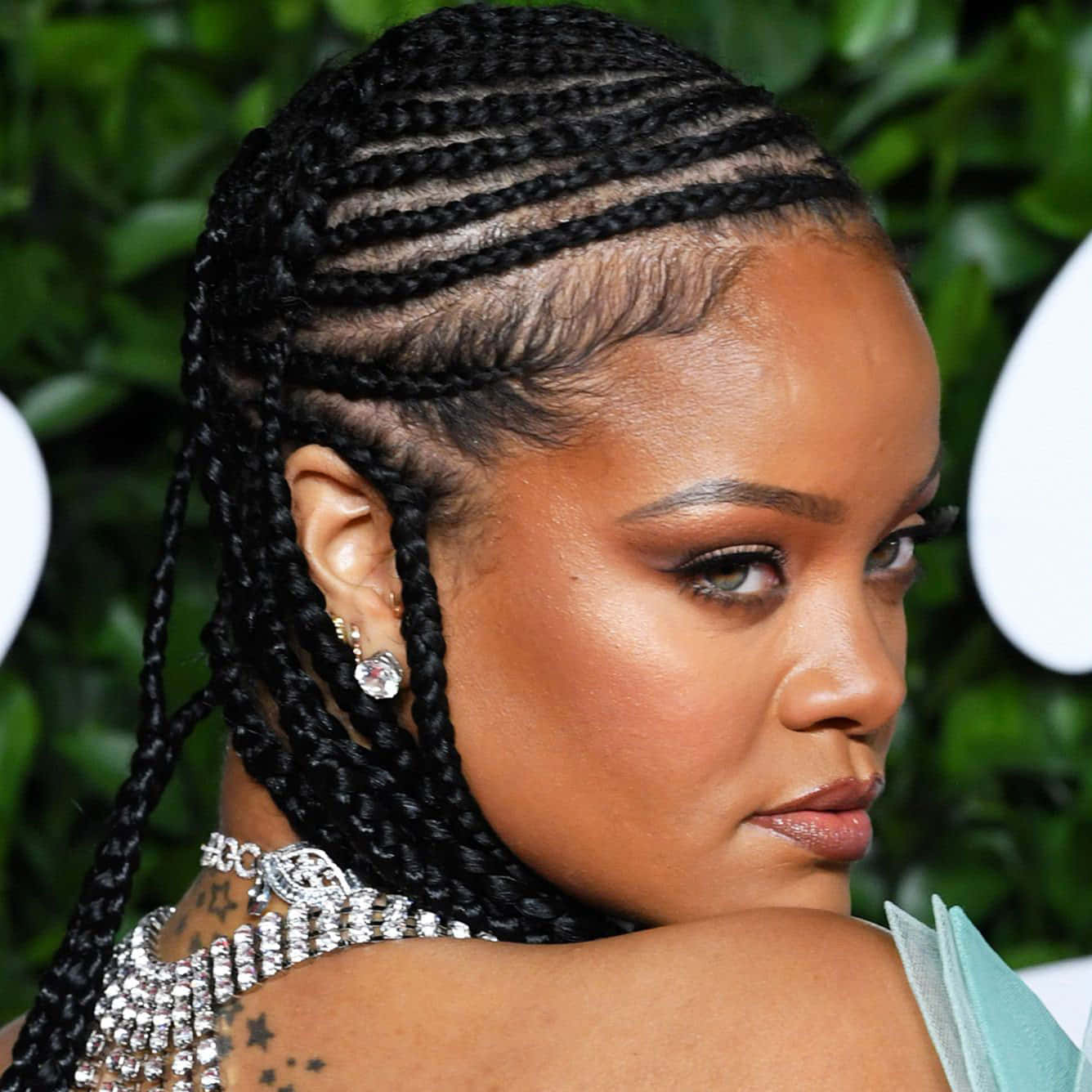 Celebrity 桌布 壁紙 — Rihanna 的近距離特寫，帶有複雜的黑色辮子、鑽石耳環和星星紋身，背景是茂密的綠色。
