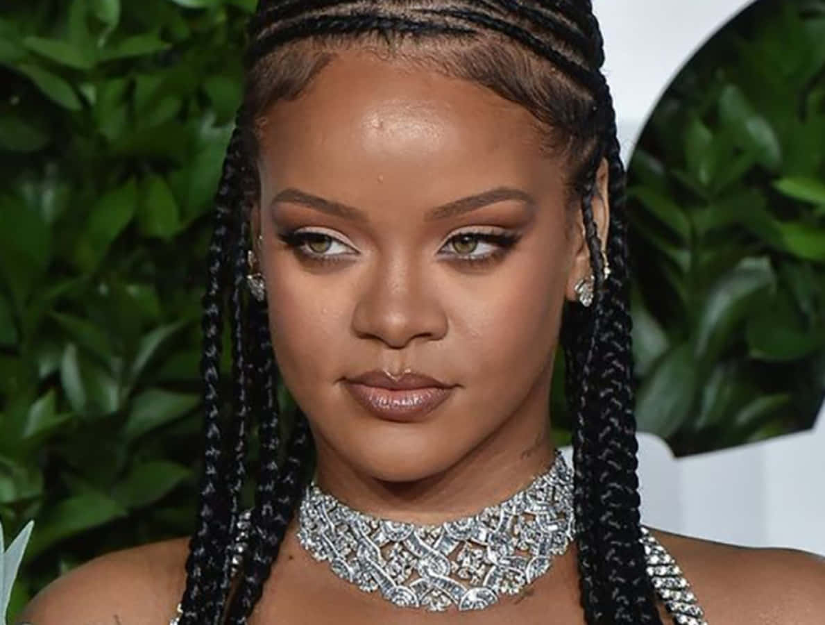 Braids Hairstyles 2022 桌布 壁紙 — Rihanna 編著辮子，戴著閃爍的鑽石頸鍊，在茂密的綠色樹葉背景下凝視。