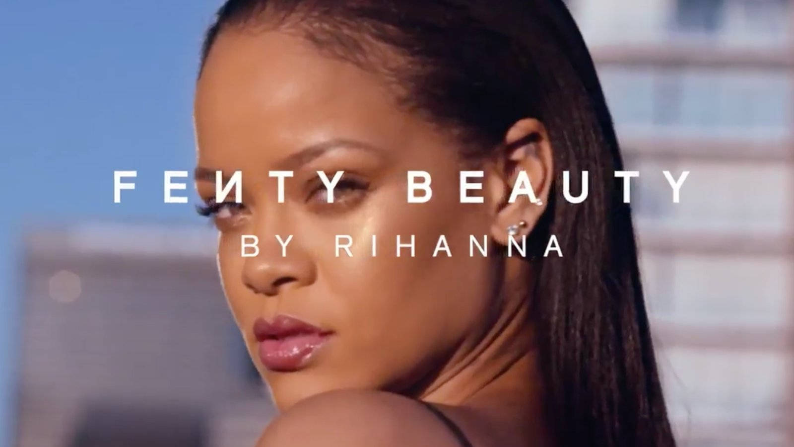 Fenty 桌布 壁紙 — Rihanna 自信地凝視著模糊的城市景觀，在明亮的日光下帶有粗體文字疊加。