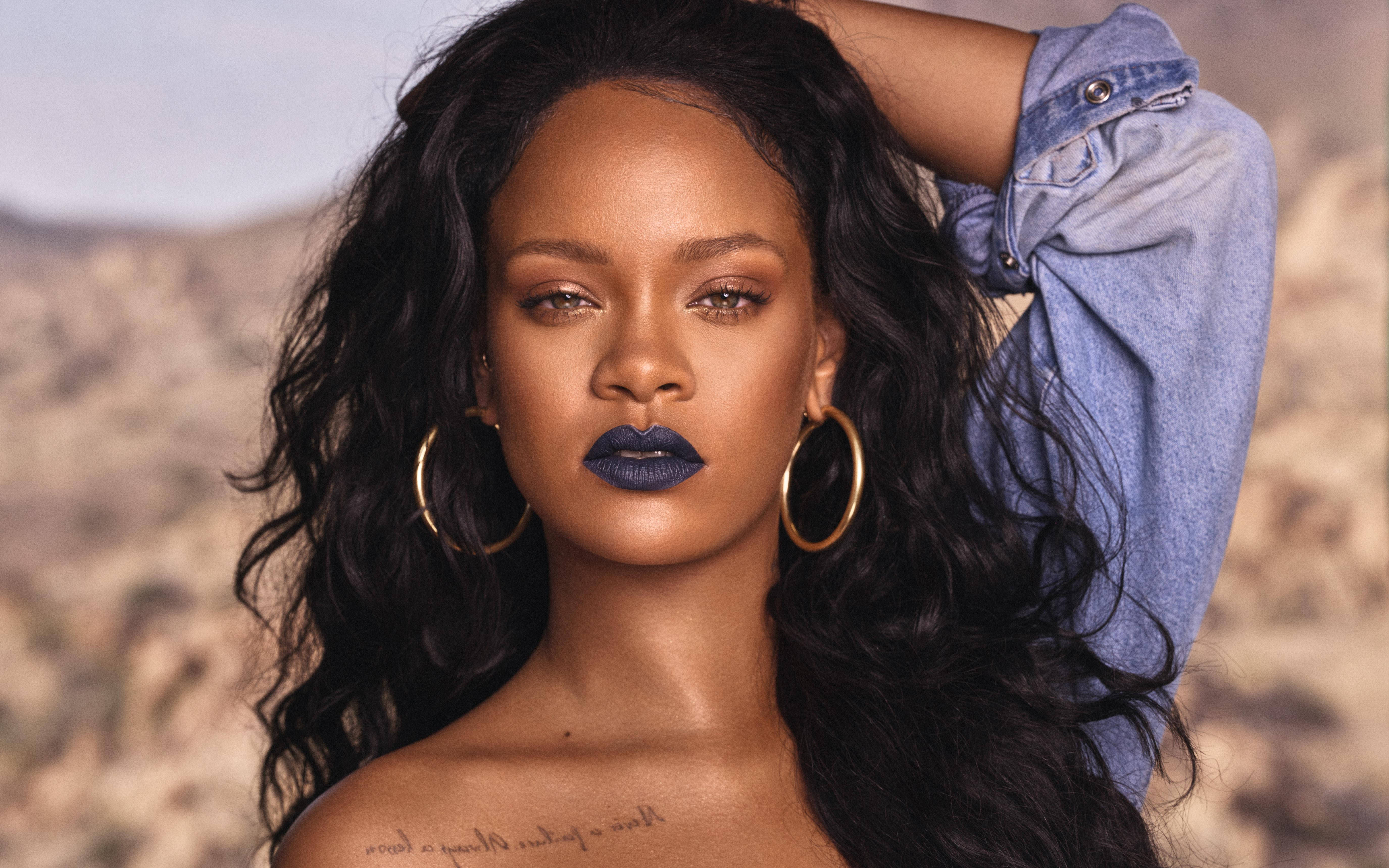 Celebrity 桌布 壁紙 — Rihanna 自信地擺姿勢，塗著深藍色唇膏，戴著金色圓環耳環，背景是模糊的沙漠。