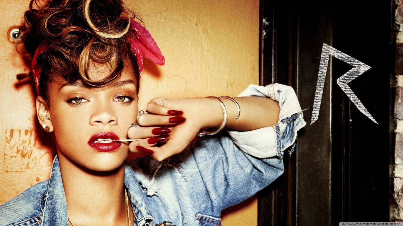 蕾哈娜 桌布 壁紙 — Rihanna 自信地穿著牛仔外套，在帶有風格化R標誌的塗鴉牆前擺姿勢。