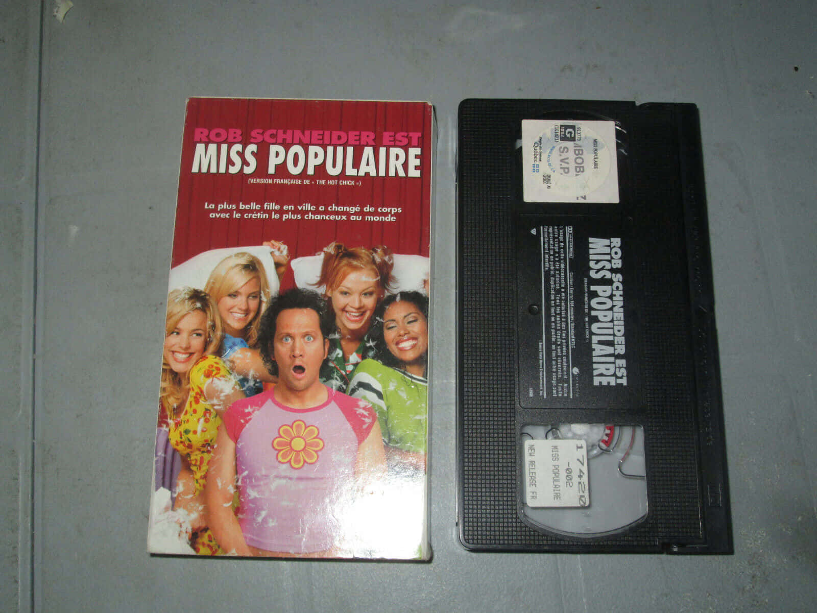 actor 桌布 壁紙 — 《Rob Schneider est Miss Populaire》的VHS錄影帶及其封套並排放在灰色表面上。