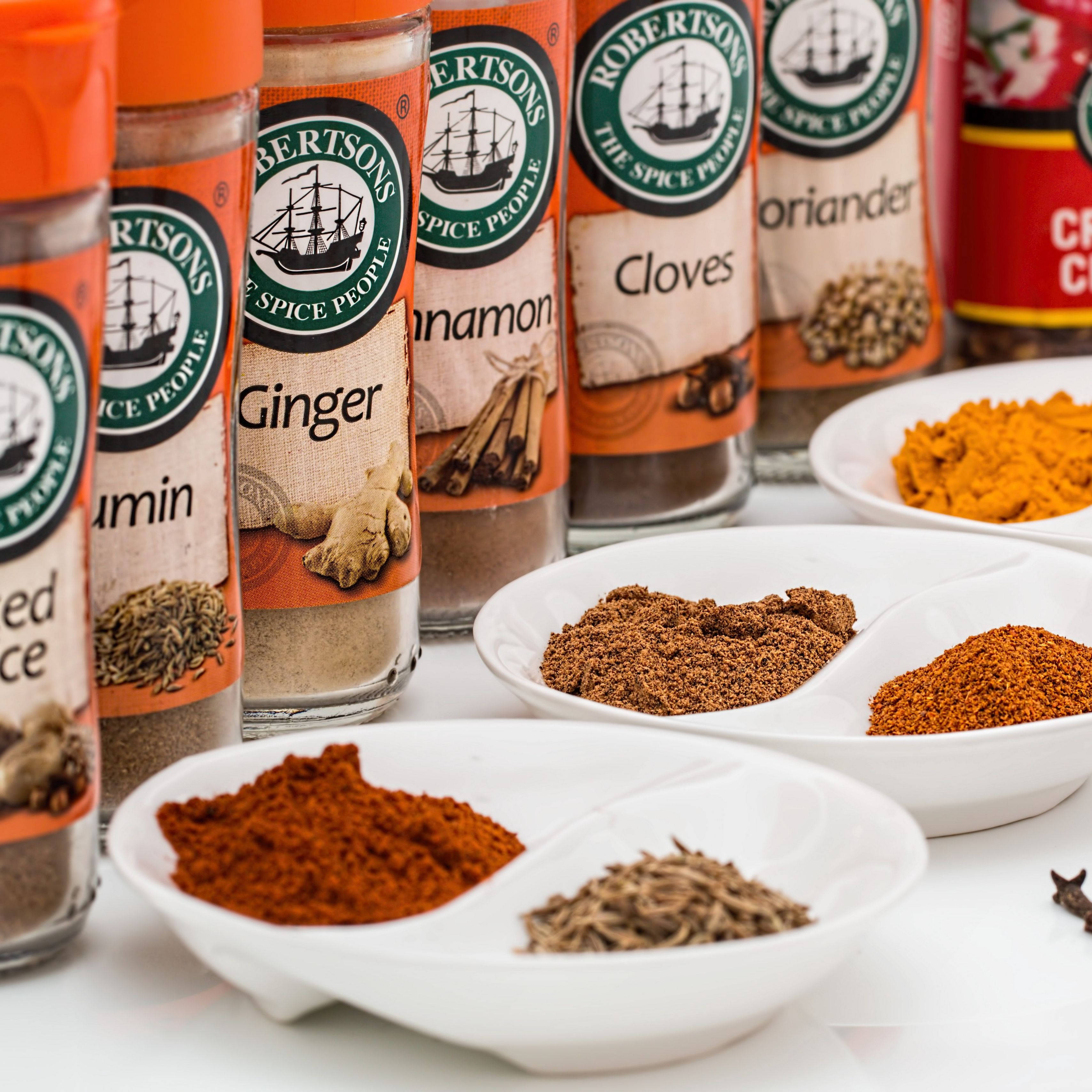 Spices 桌布 壁紙 — Robertson香料瓶和碗的特寫，裝滿了色彩繽紛的磨碎香料，如生薑、肉桂和薑黃，放在乾淨的白色表面上。