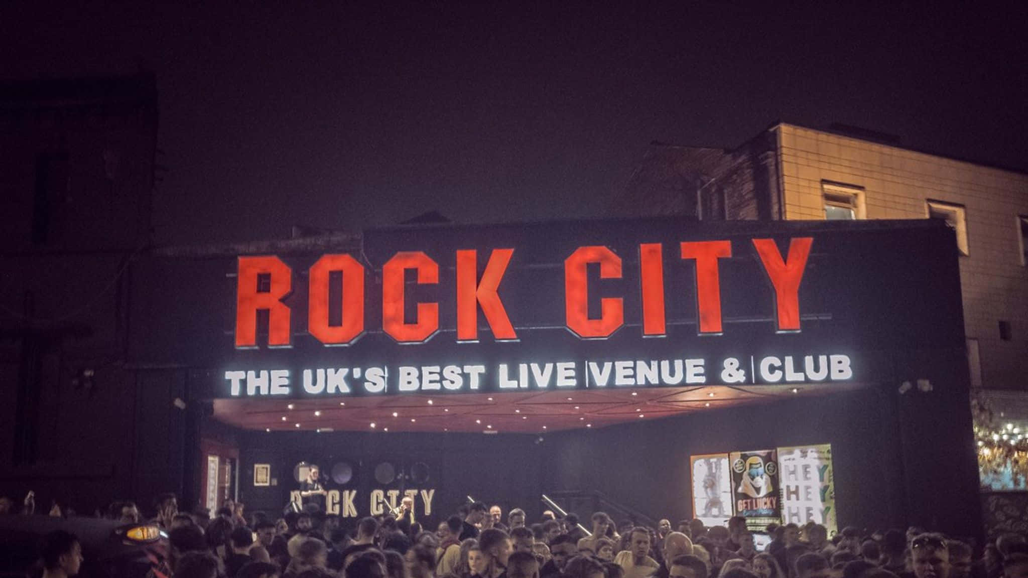 桌布 壁紙 — Rock City 場地的充滿活力的夜景，帶有發光的紅色標誌和下方聚集的密集人群。