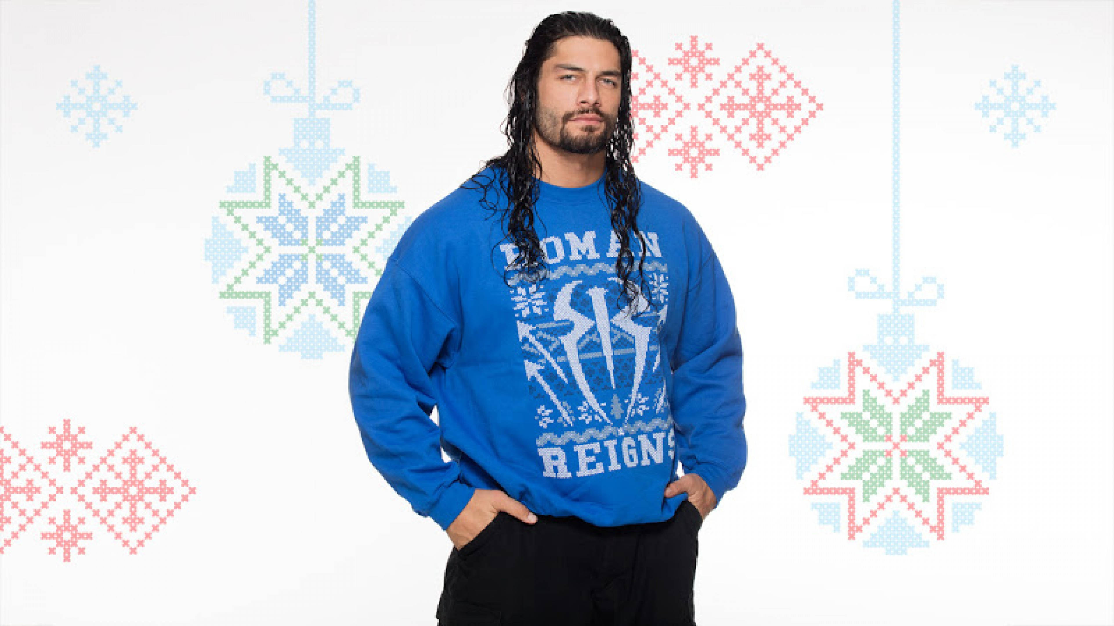 Roman 桌布 壁紙 — Roman Reigns 自信地站在白色背景前，身穿藍色節日毛衣，背景裝飾著像素化飾物。