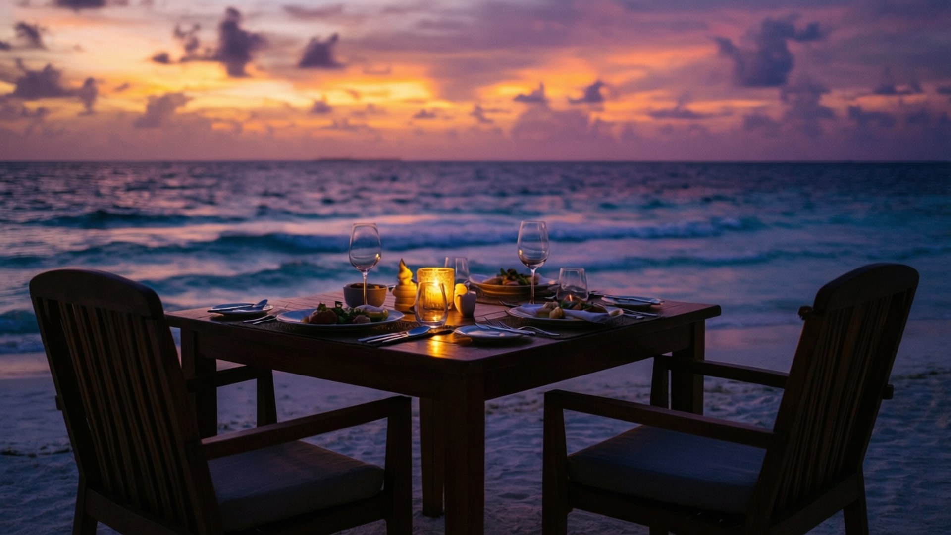 Beach Candlelight Dinner 壁紙 — 日落時分，沙灘上擺放著一張二人木桌，桌上燭光搖曳，紅酒杯閃爍，天空呈現鮮豔的橙色、紫色和藍色，海浪拍打著海岸。