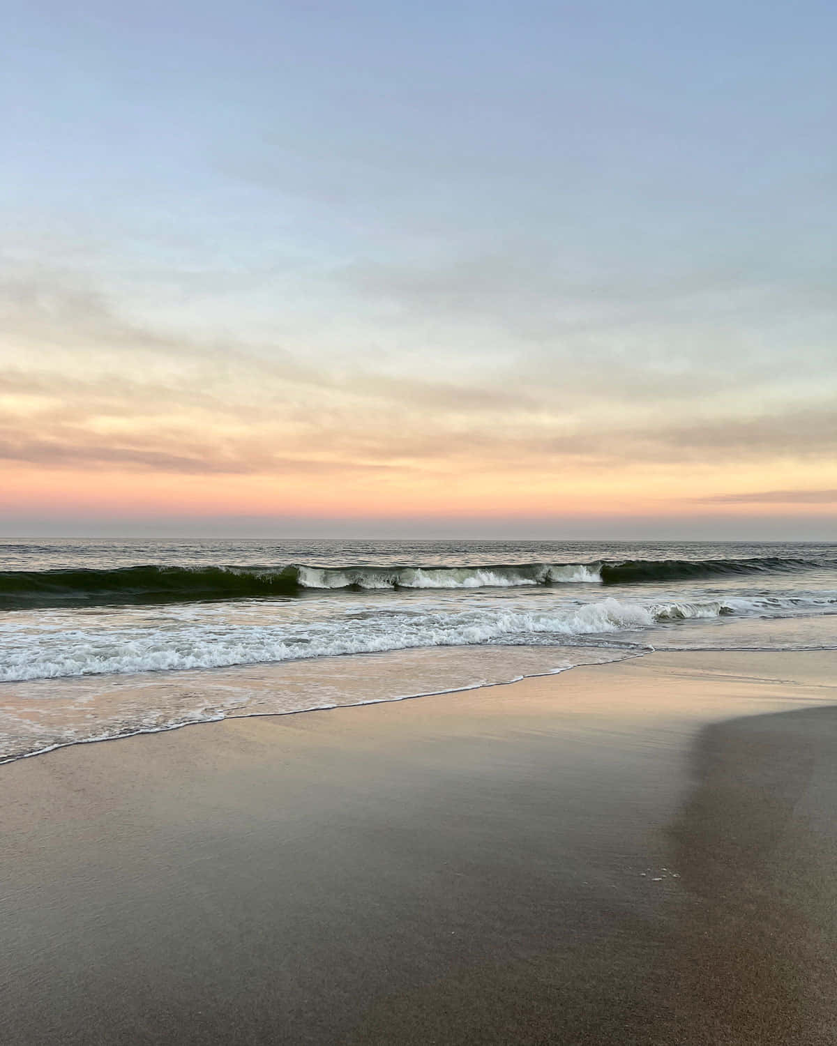Coastal Granddaughter 桌布 壁紙 — 柔軟的海浪在粉彩色的日落天空和柔和雲朵下，拍打著濕潤的沙灘。