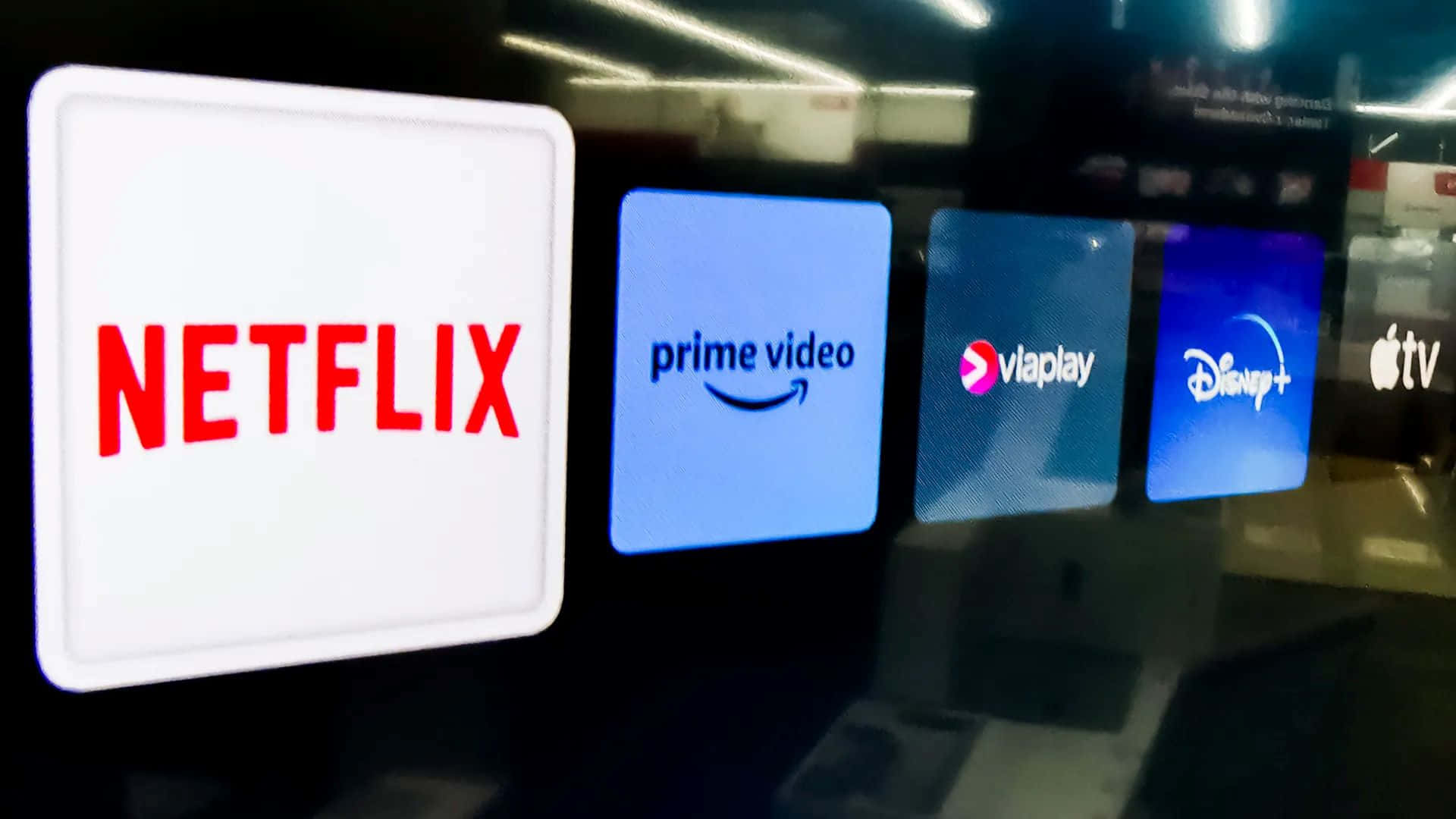  壁紙 — 一排發光的串流服務標誌，包括 Netflix、Prime Video、Viaplay、Disney+ 和 Apple TV，顯示在昏暗的現代室內屏幕上。