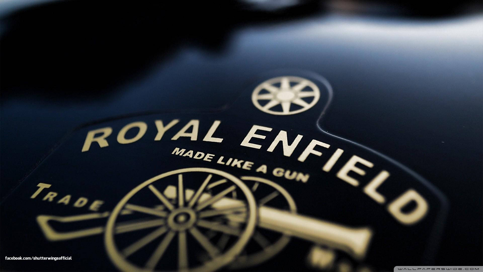 Royal 桌布 壁紙 — Royal Enfield 摩托車標誌的特寫，金色字體和大炮徽章在光澤黑色表面上。