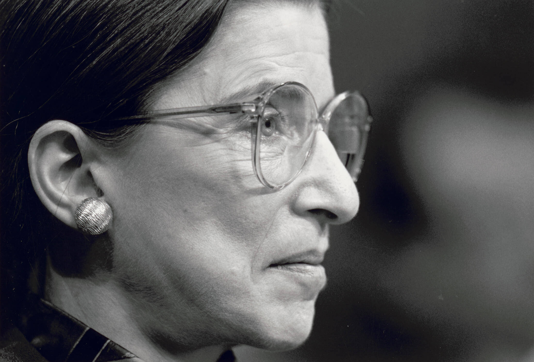 Ruth Bader Ginsburg 桌布 壁紙 — Ruth Bader Ginsburg 的側面黑白特寫肖像，戴著眼鏡和獨特的耳環。