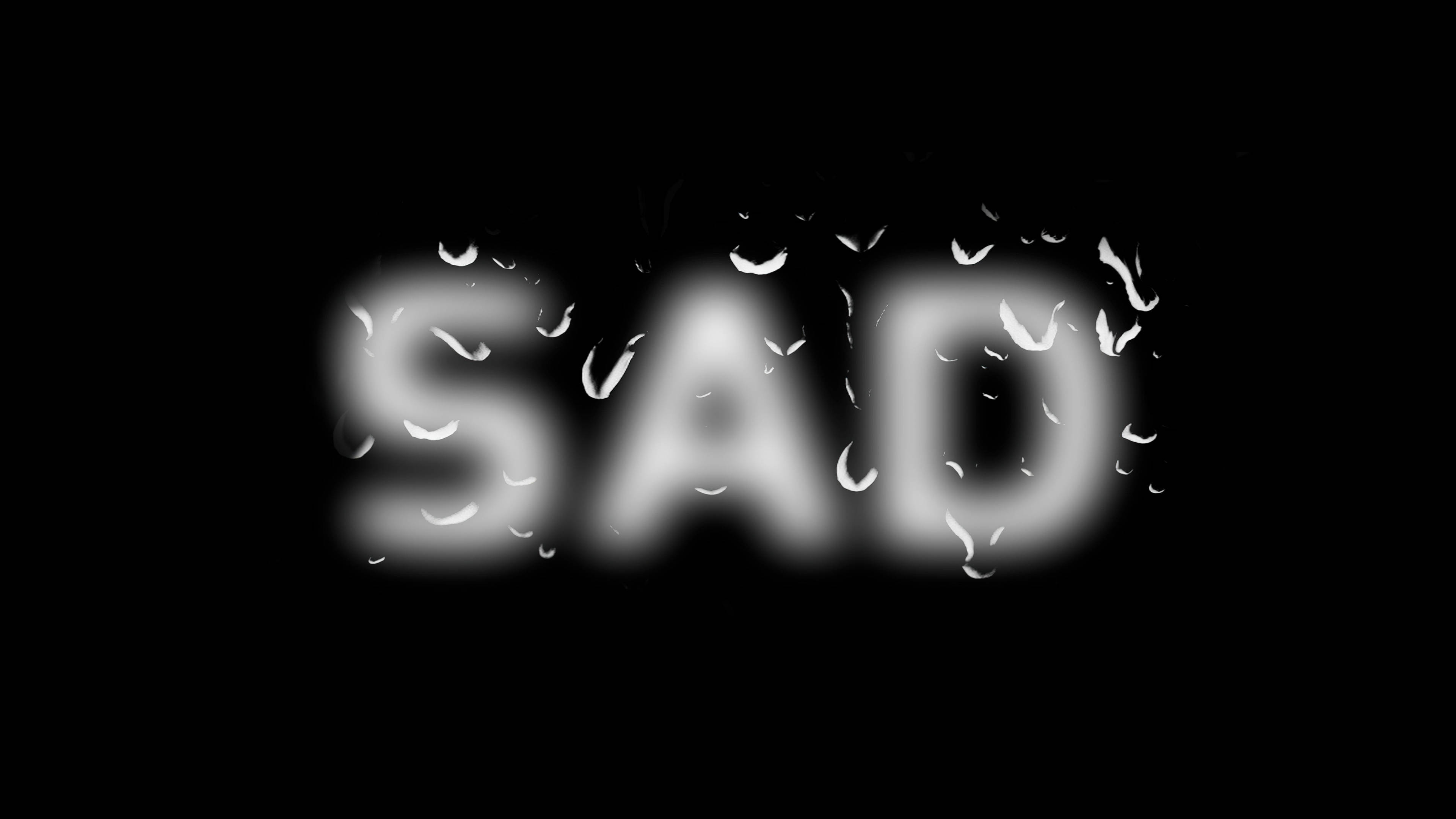 Raindrops 桌布 壁紙 — 「SAD」這個字在黑色背景上柔和地發光，雨滴附著在模糊的字母上。
