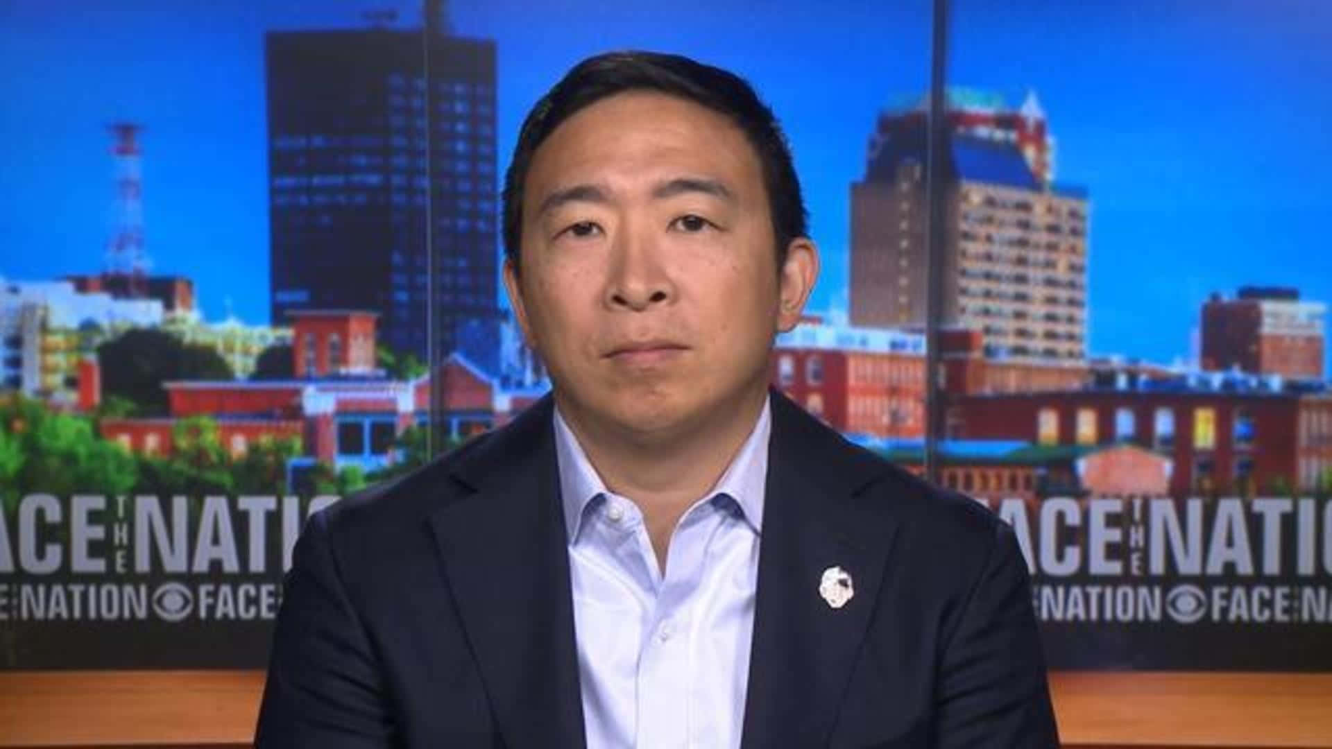 美國 桌布 壁紙 — 一名身穿深色西裝和淺藍色襯衫的男子坐在城市天際線背景前，帶有「Face the Nation」品牌標誌。