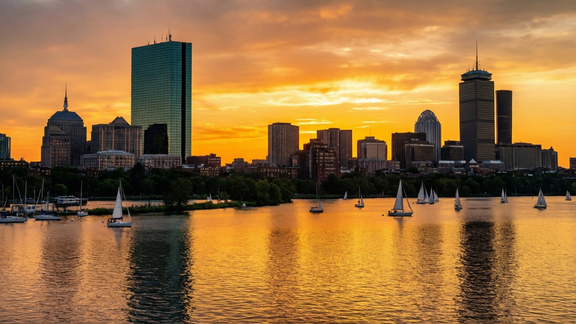 Boston Skyline Sunset 壁紙 — 帆船在金色的水面上滑行，水面倒映著現代城市天際線後熾熱的日落。