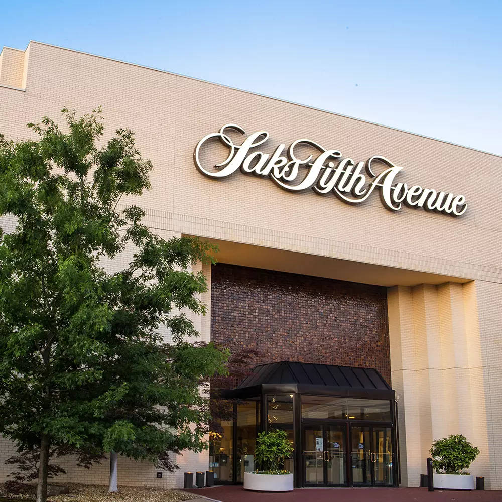 Building 桌布 壁紙 — Saks Fifth Avenue 商店外牆，米色磚牆、綠樹和玻璃門，在清澈藍天下。