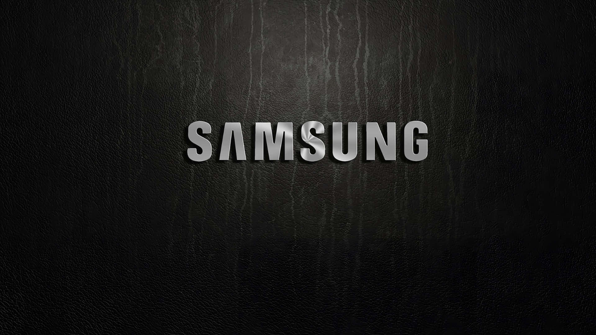  壁紙 — Samsung 標誌以金屬銀色字體居中顯示，背景為帶有細微垂直紋理的黑色皮革紋理。