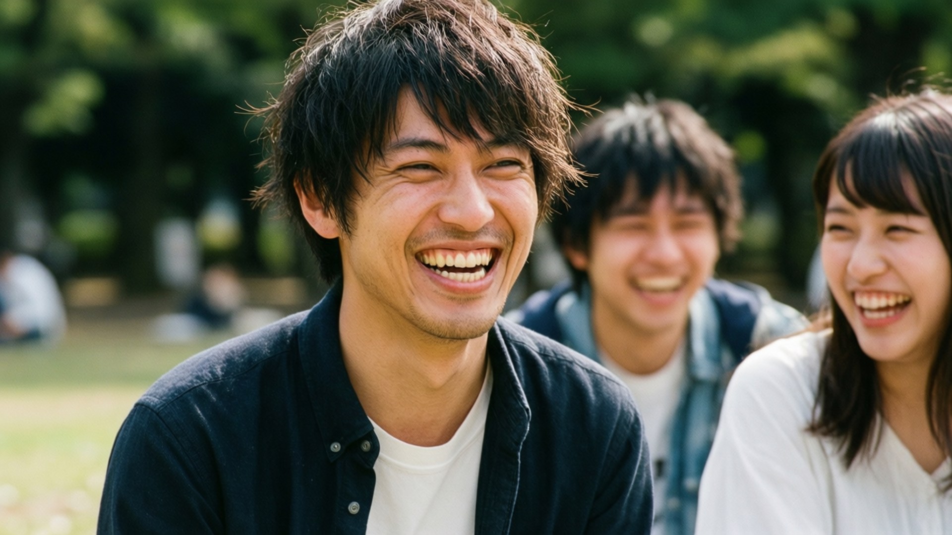 Joyful Laugh 壁紙 — 三個微笑的年輕成年人在陽光明媚的公園裡一起大笑，身後有綠樹。
