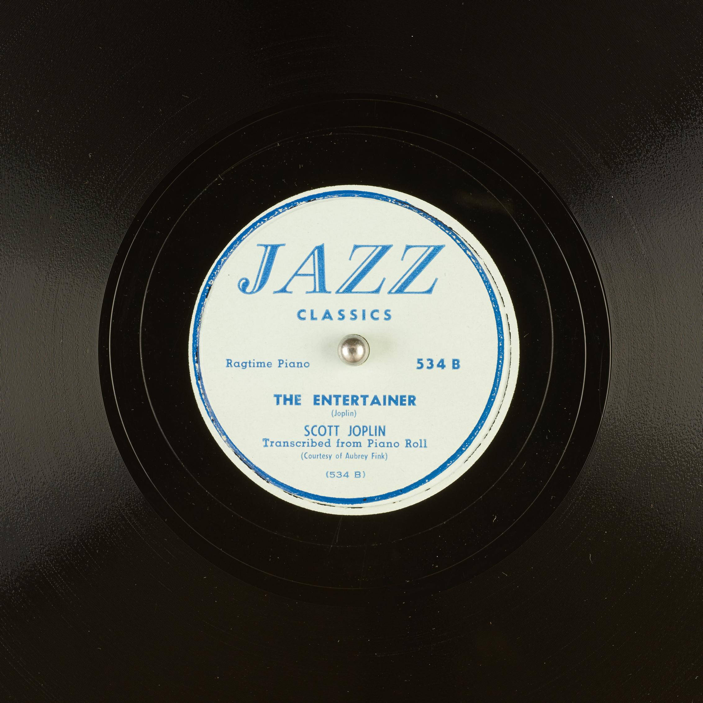song 桌布 壁紙 — Scott Joplin 的《The Entertainer》以粗體藍色文字印在白色中心上的復古爵士黑膠唱片標籤特寫。