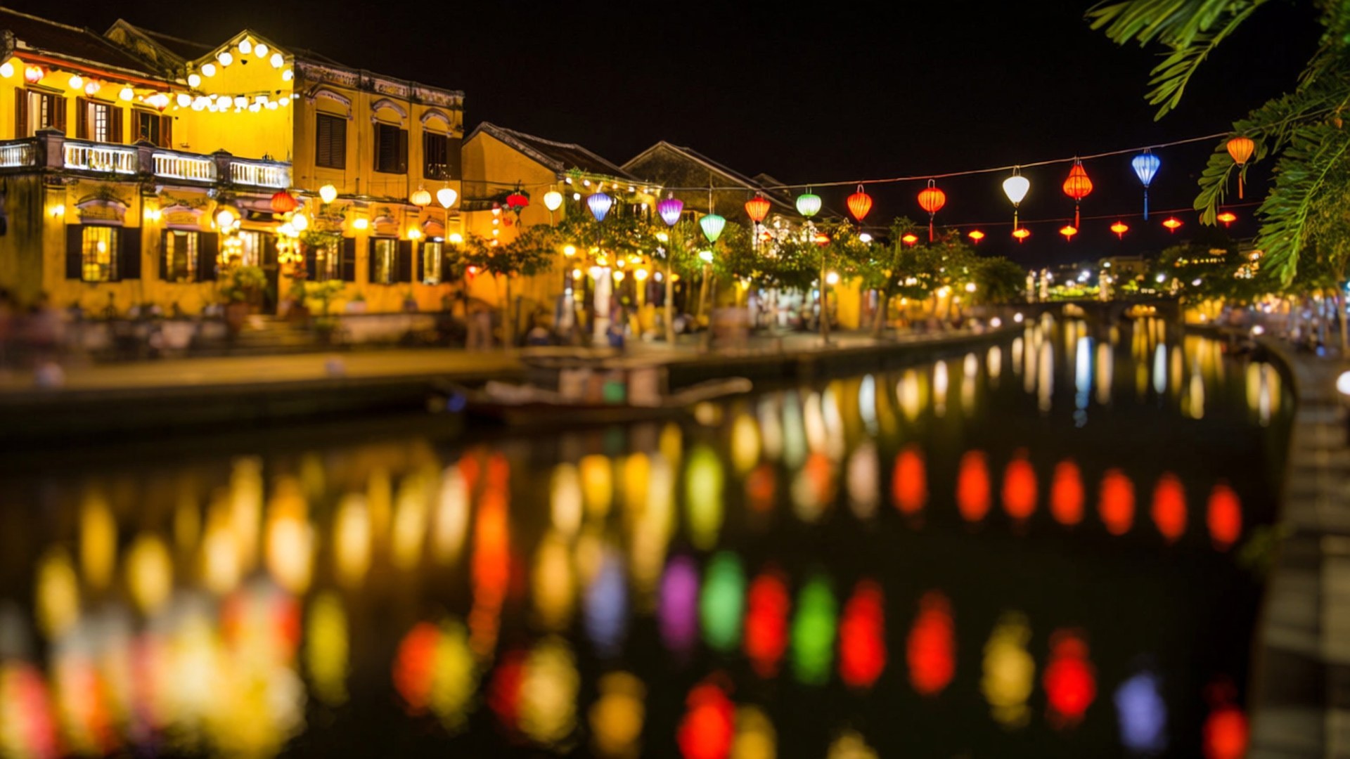 Hoi An Lantern Night 壁紙 — 色彩繽紛的燈籠在夜間照亮運河，它們的倒影在歷史建築旁的水面上閃爍。