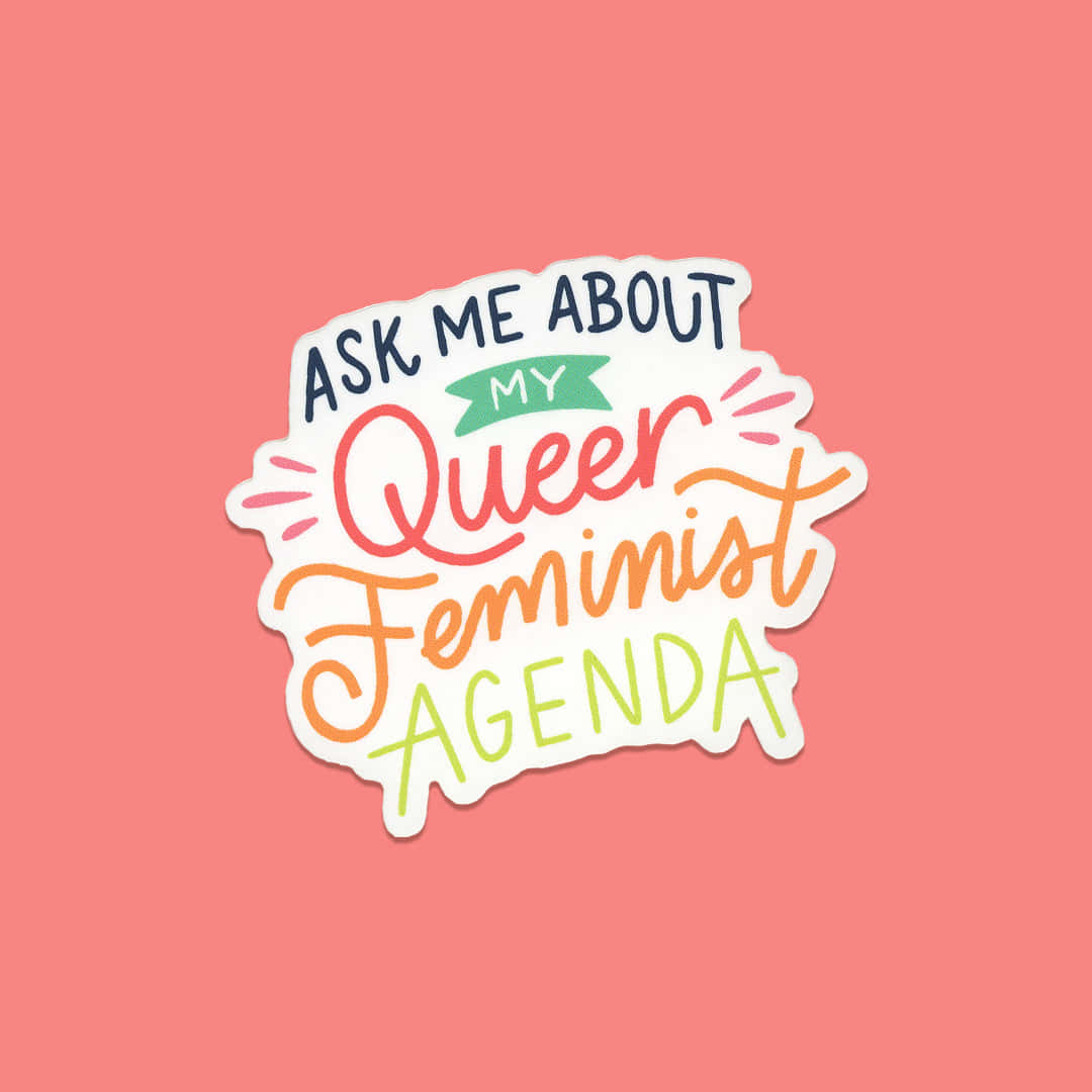  壁紙 — 一個色彩繽紛的手寫貼紙，上面寫著「Ask Me About My Queer Feminist Agenda」，背景為珊瑚粉紅色。