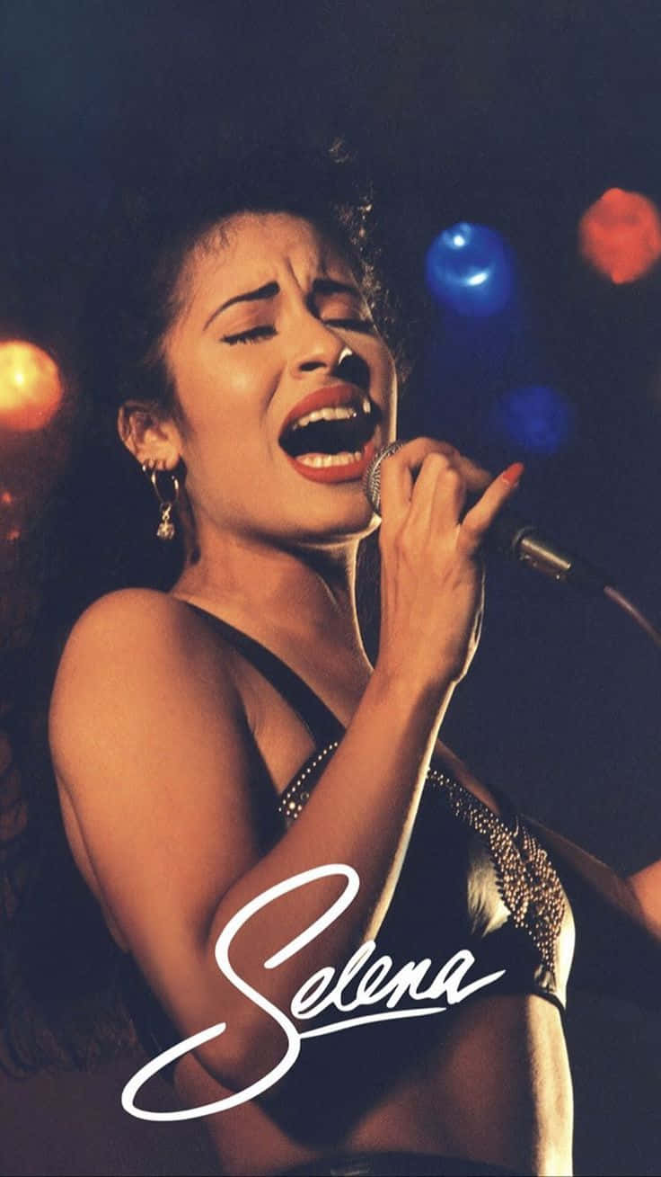 Selena Quintanilla iPhone 桌布 壁紙 — Selena Quintanilla 在色彩繽紛的舞台燈光下熱情地對著麥克風唱歌，她的名字寫在下方。