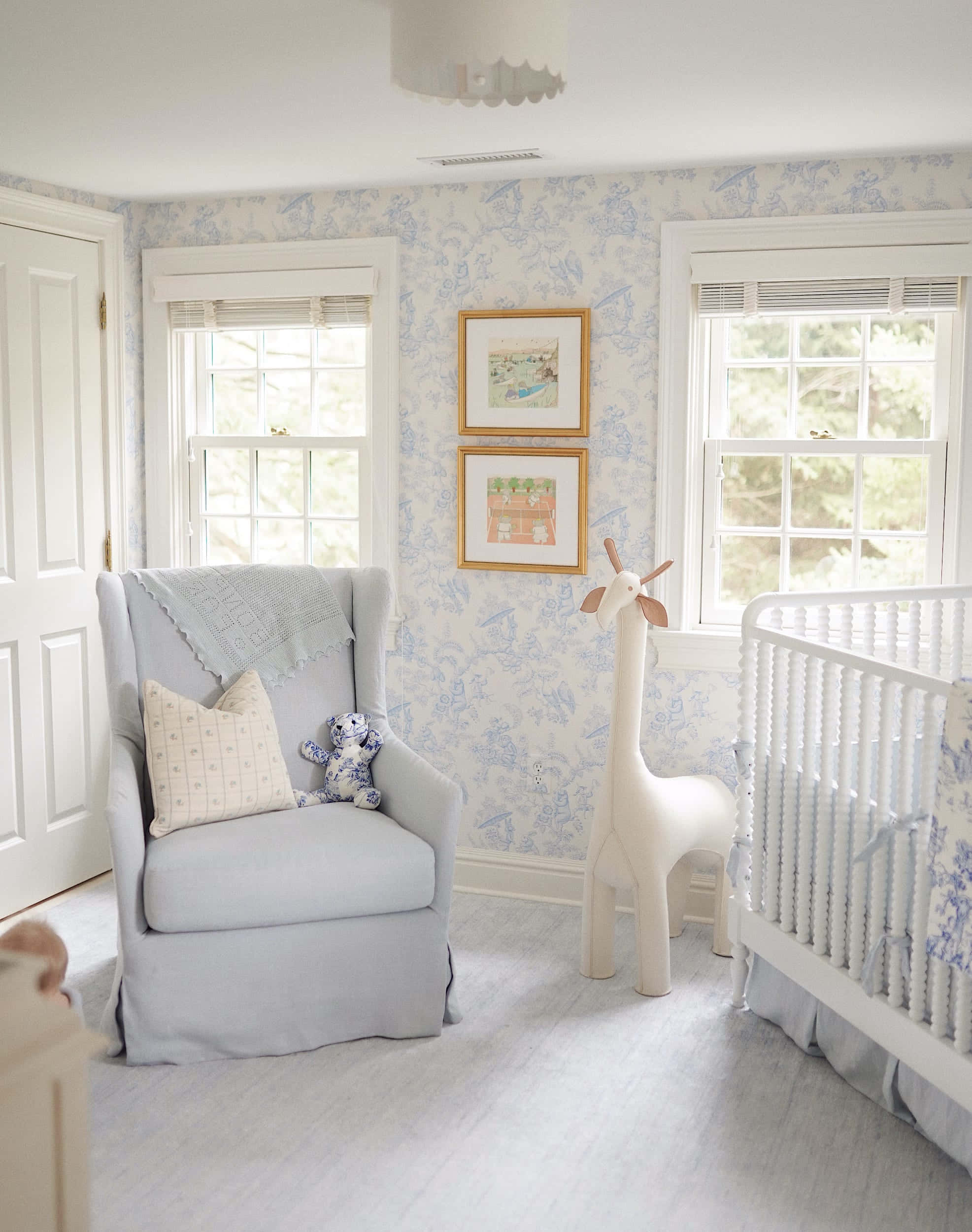 Nursery 桌布 壁紙 — 寧靜的嬰兒房，配有淺藍色 toile 壁紙、白色嬰兒床和扶手椅，窗戶透入自然光。