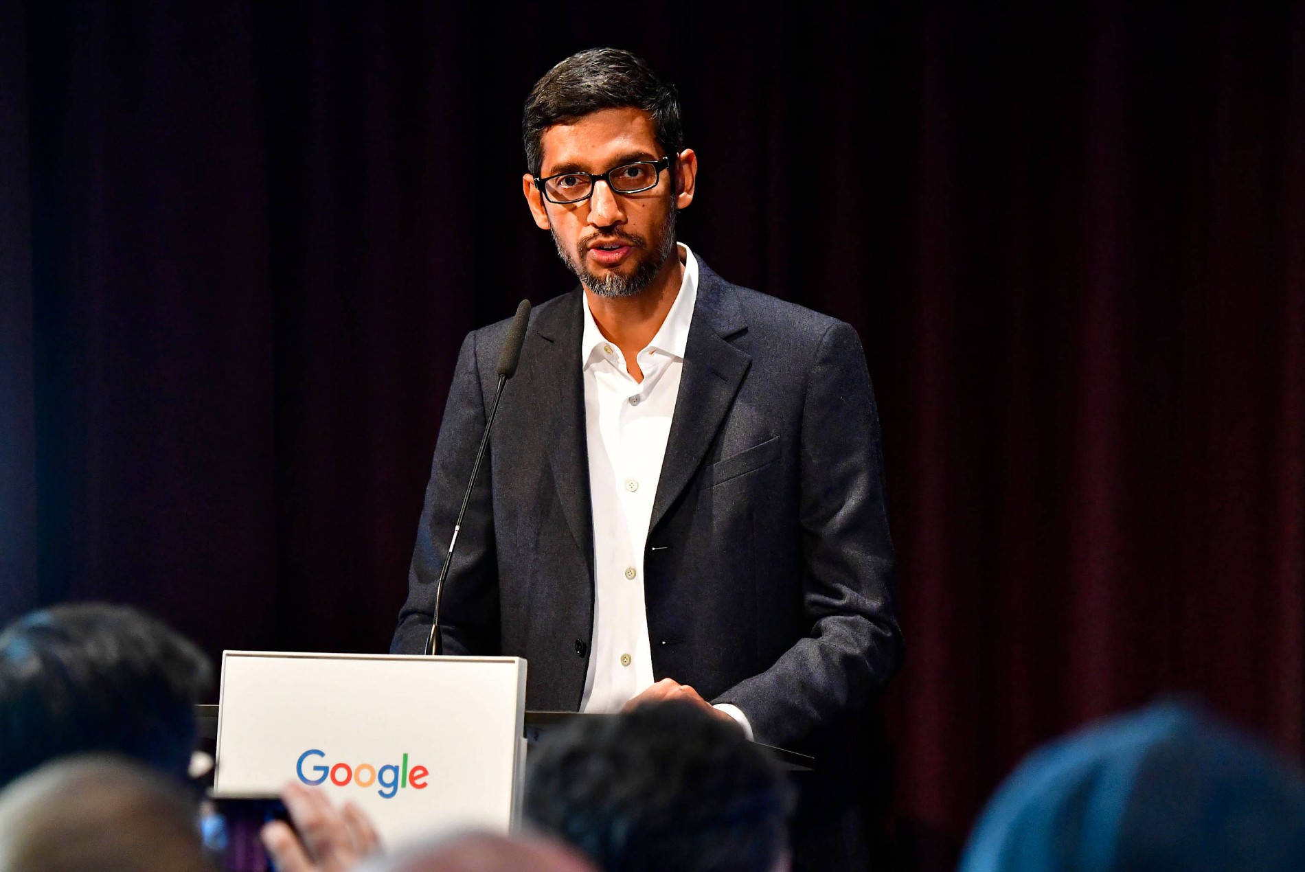 google 桌布 壁紙 — Sergey Brin 在Google活動中戴著眼鏡和深色西裝，背景是深紅色窗簾。