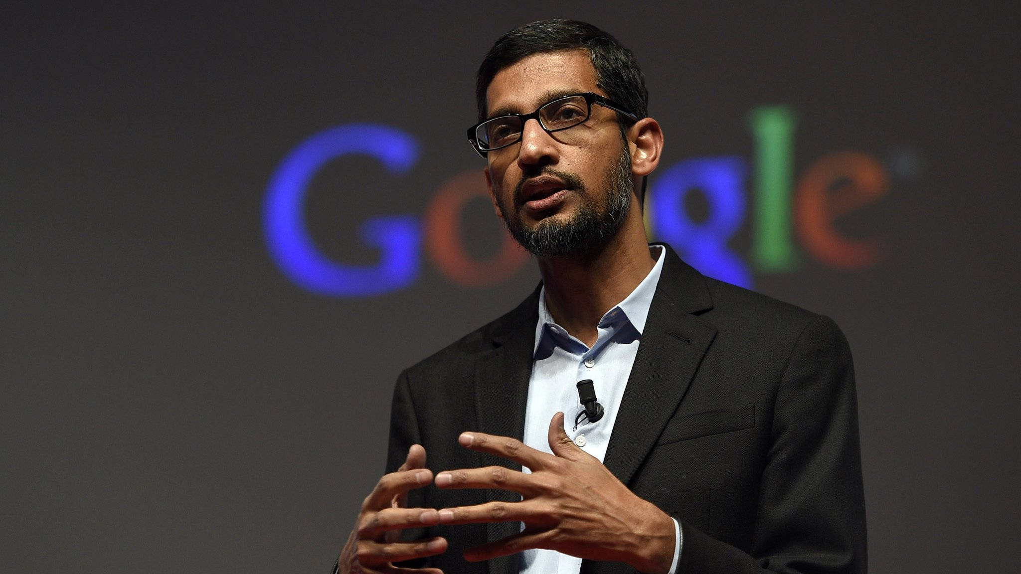 google 桌布 壁紙 — Sergey Brin 在Google活動中發言，背後有色彩繽紛的模糊標誌。