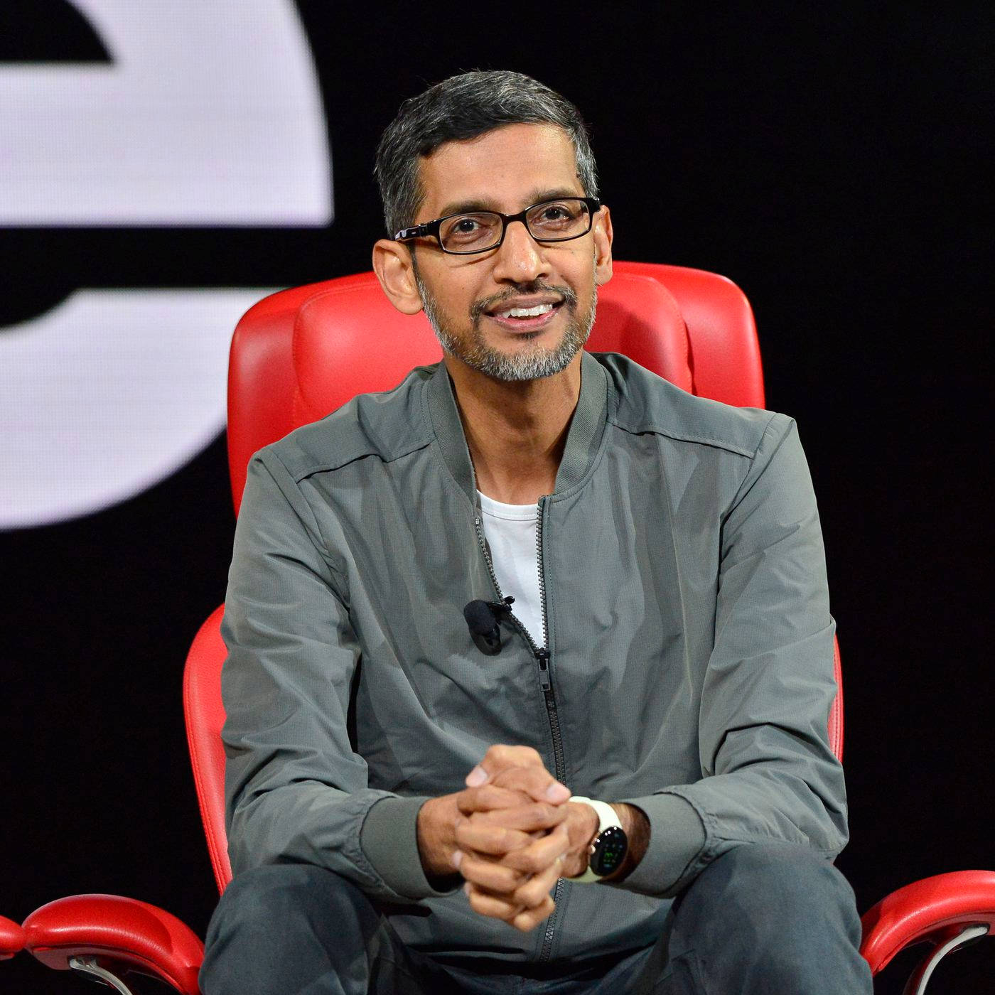 google 桌布 壁紙 — Sergey Brin 微笑著坐在紅色椅子上，戴著眼鏡和灰色外套，背景為深色，有一個大的白色標誌。