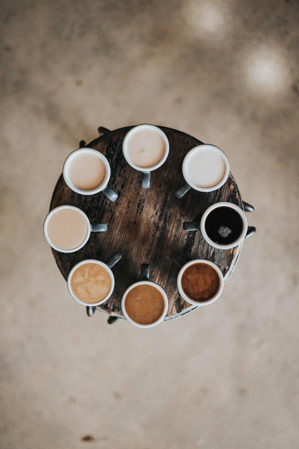 咖啡動圖 桌布 壁紙 — Top-down view of seven coffee mugs arranged in a circle on a rustic wooden table with textured concrete floor.