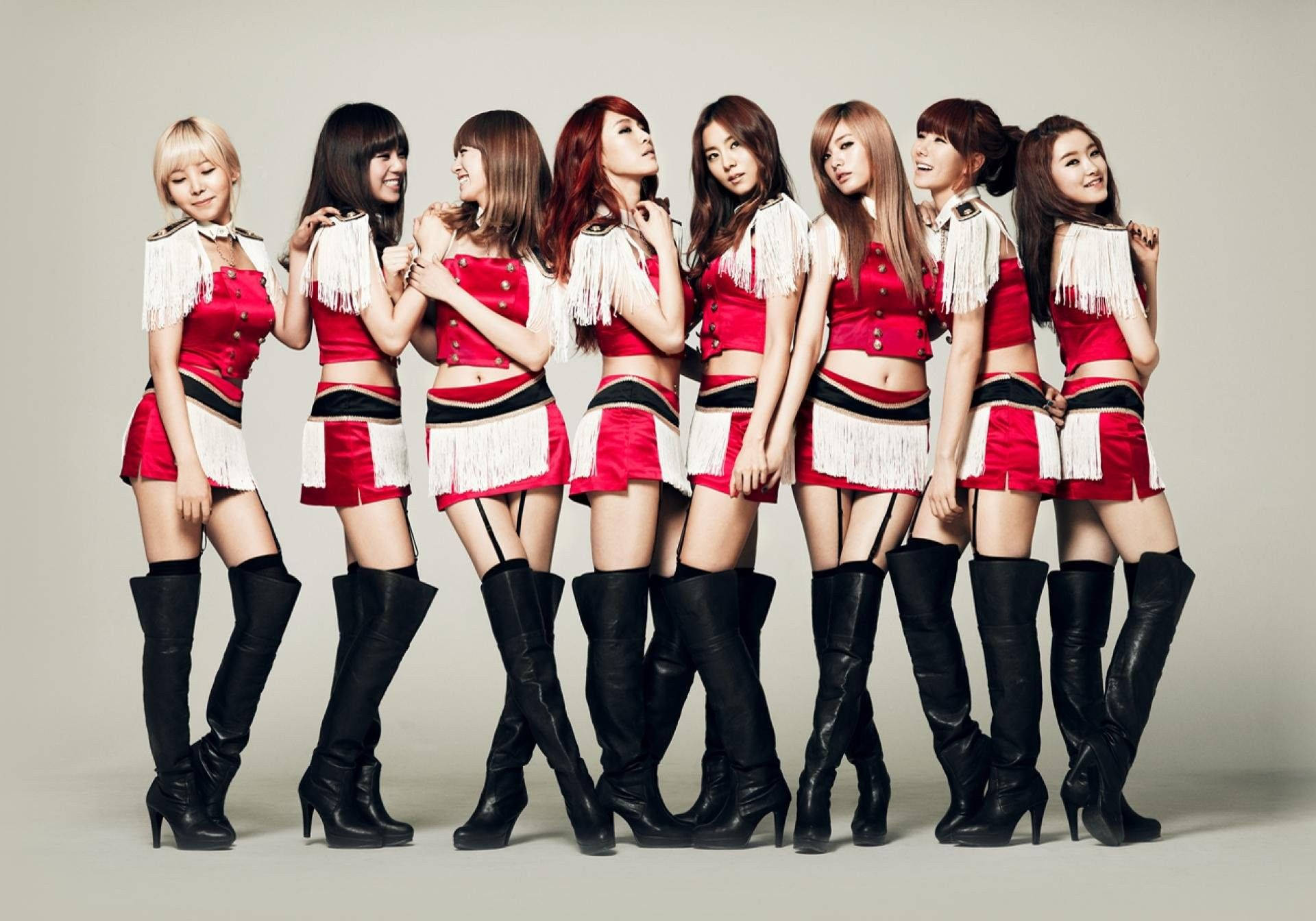 七位女性穿著紅色流蘇服裝和黑色靴子在工作室中擺姿勢。 — K Pop 壁紙