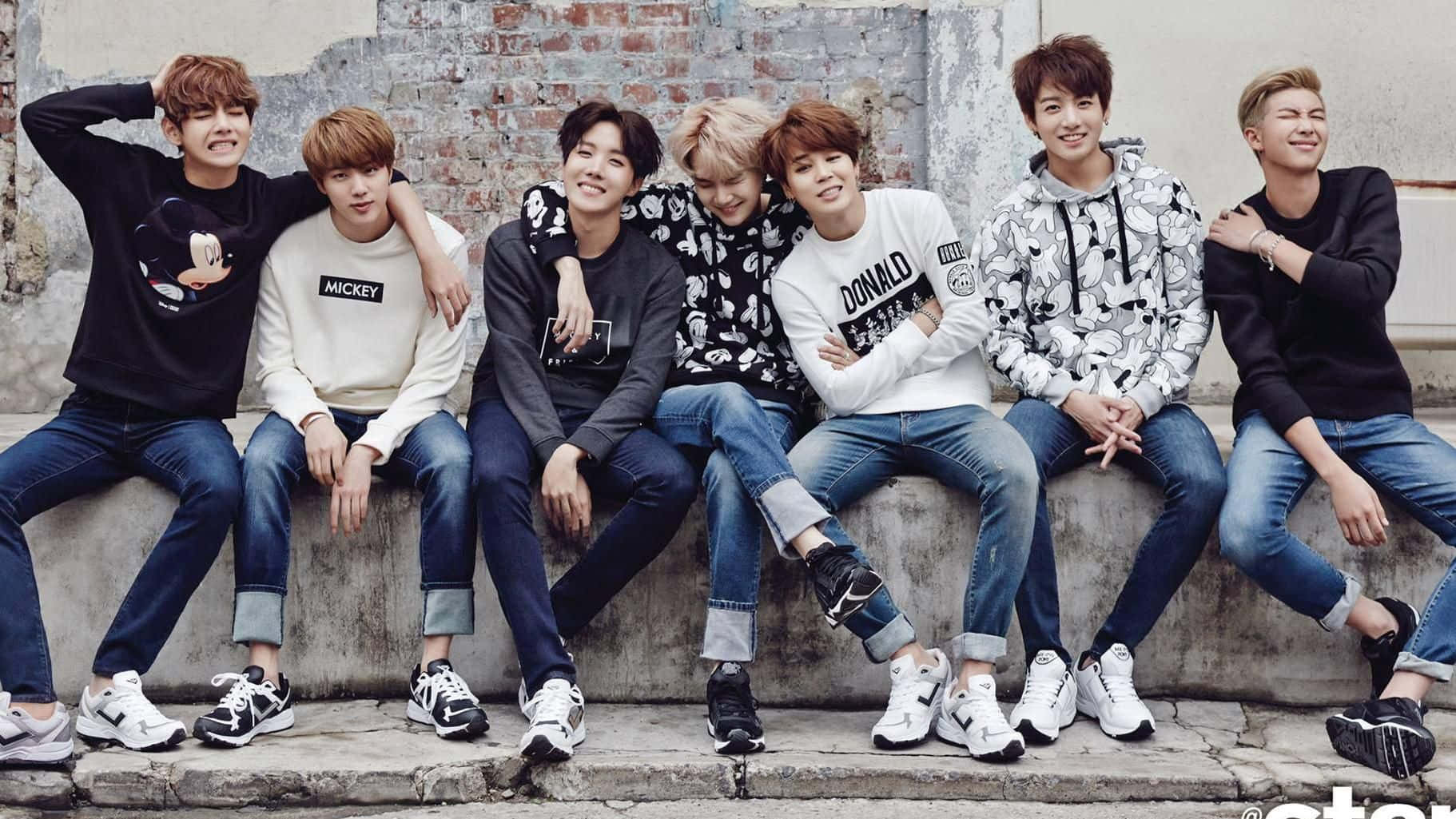 七位年輕男士身穿休閒服裝，在磚牆前坐在混凝土邊緣上。 — Bts 壁紙