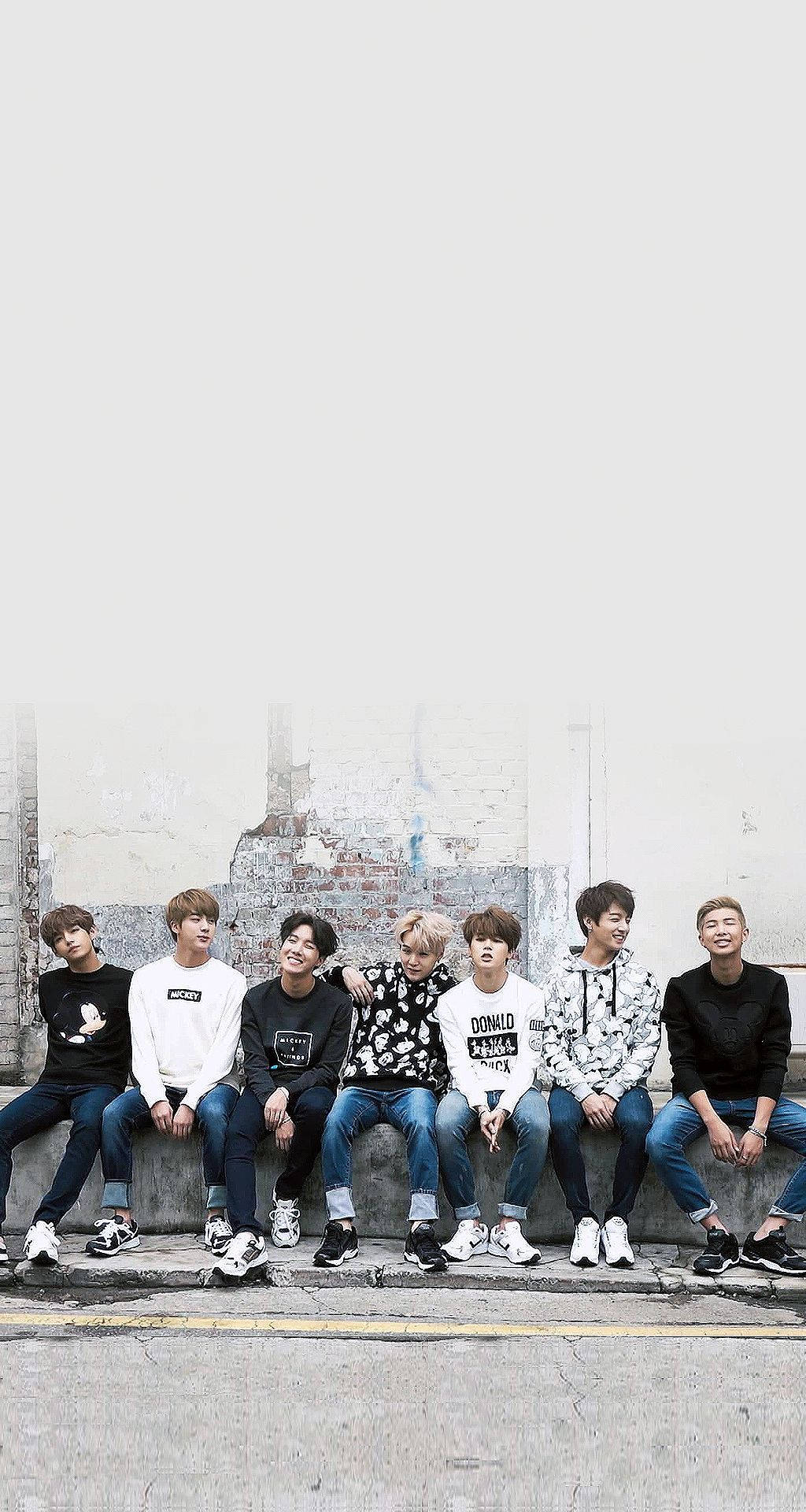 七位身穿休閒服的年輕男性坐在混凝土邊緣上，背景是磚牆。 — Bts 壁紙