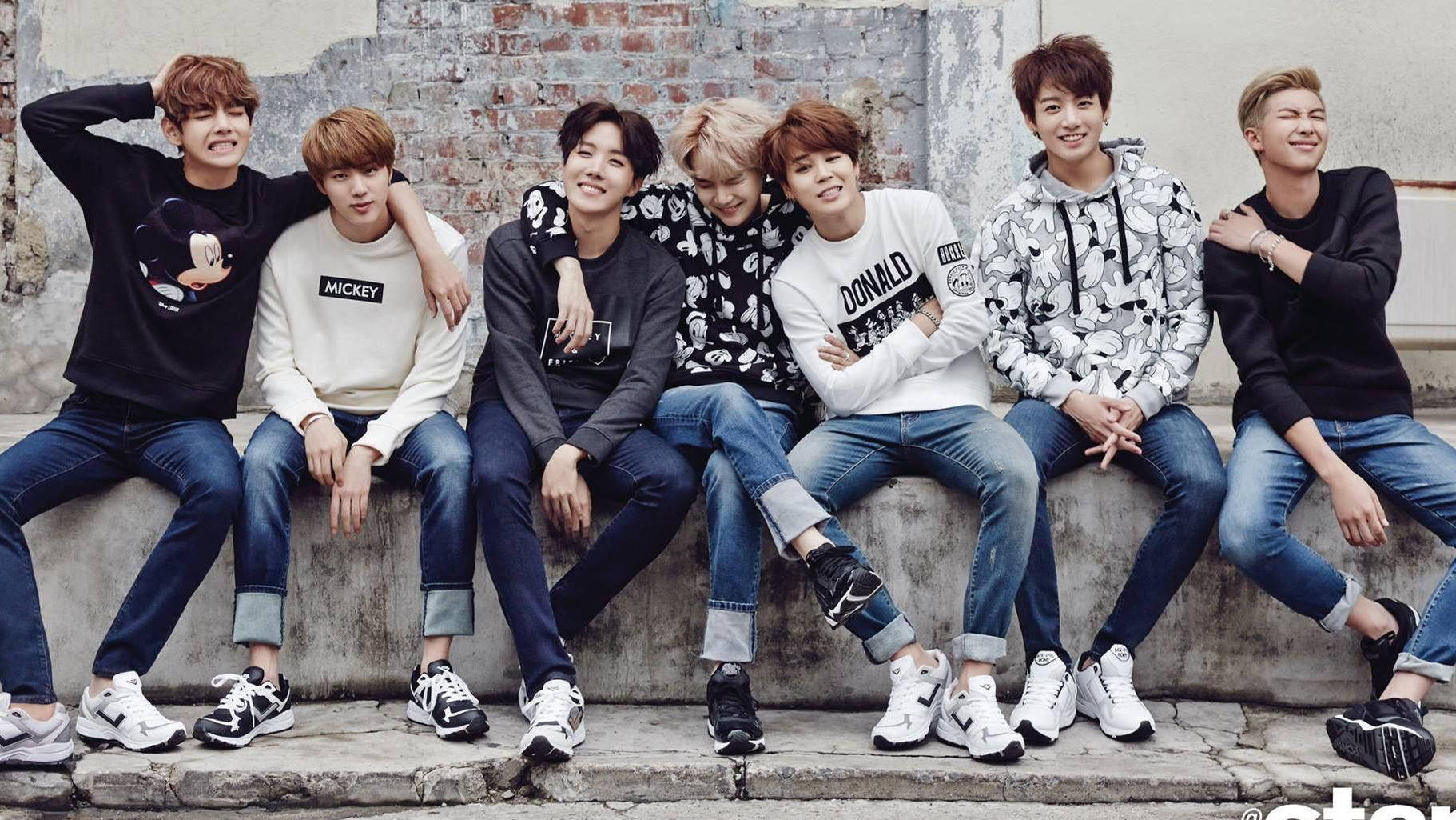 七個年輕男子身穿休閒服裝，坐在混凝土邊緣上，背靠磚牆。 — Bts 壁紙
