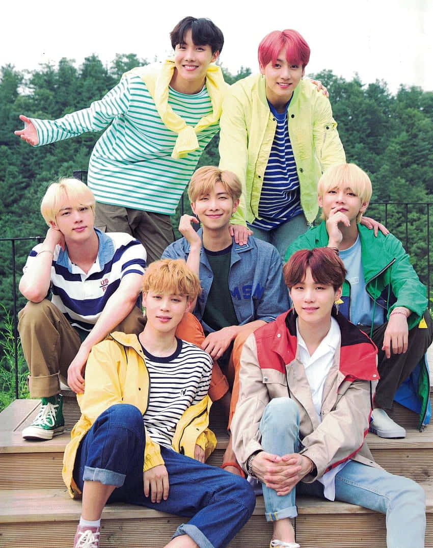 七名身穿彩色外套的年輕男子在森林中的木質台階上擺姿勢。 — Bts 壁紙